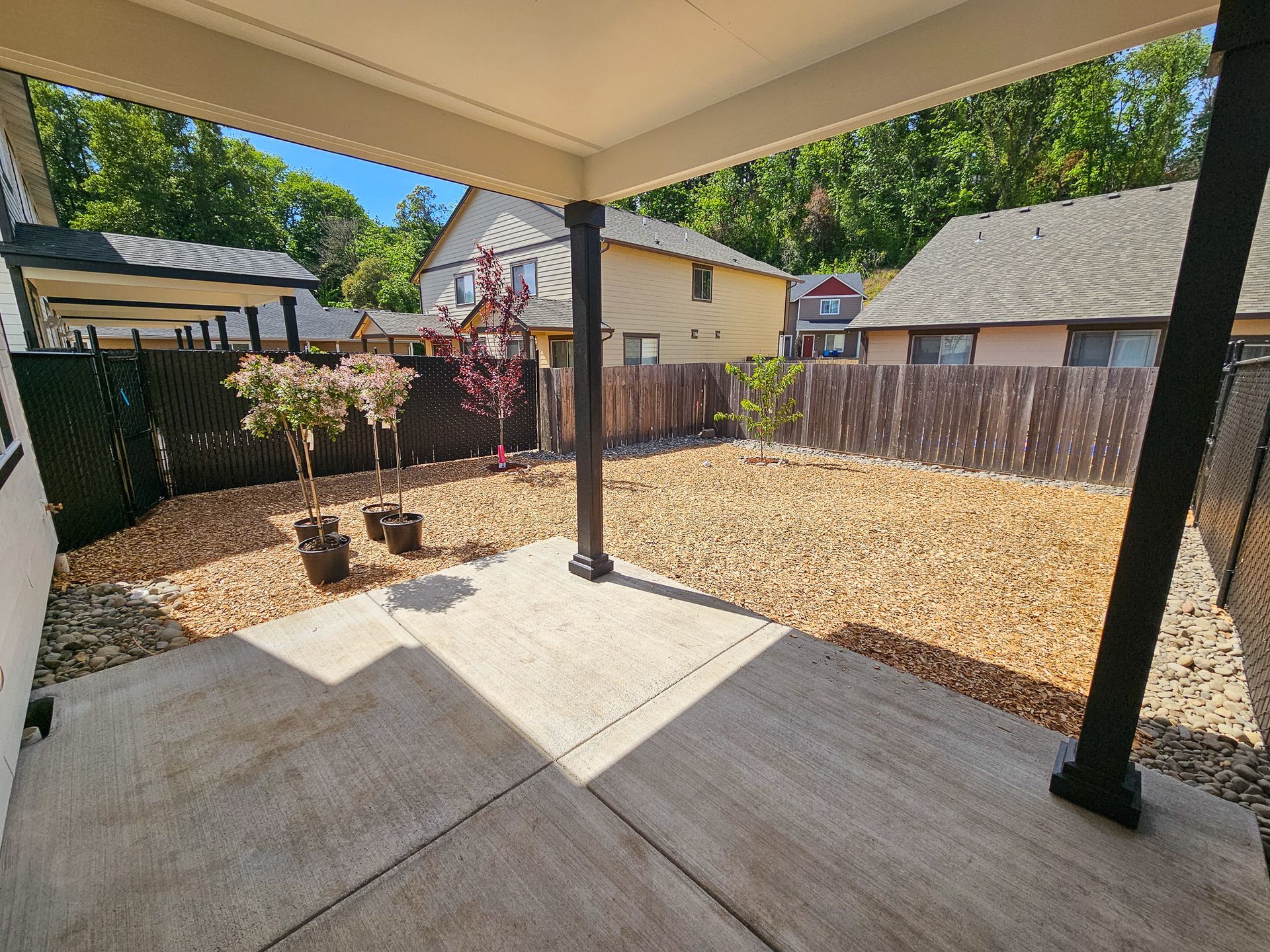 A patio with a fence and trees in the backyard of a house.