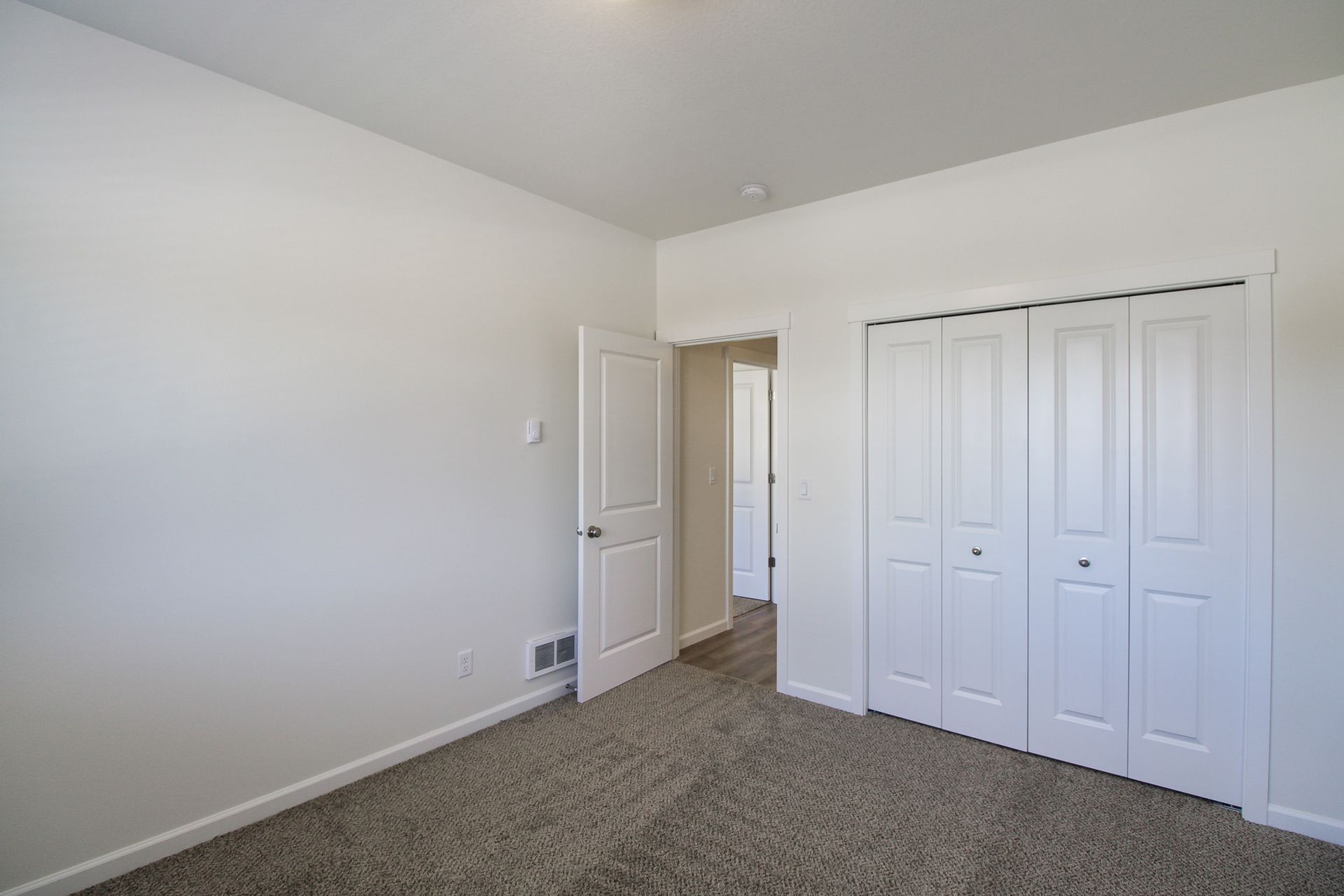 An empty bedroom with a carpeted floor and white walls and closets.