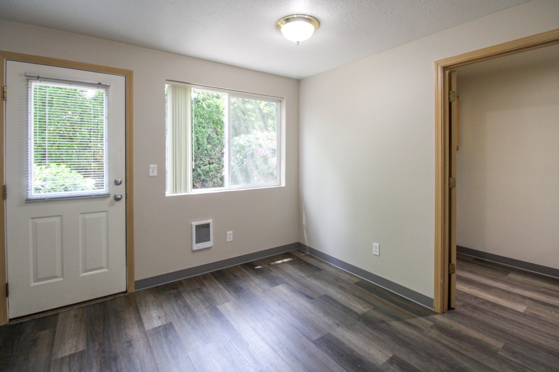 An empty room with hardwood floors , a window and a door.