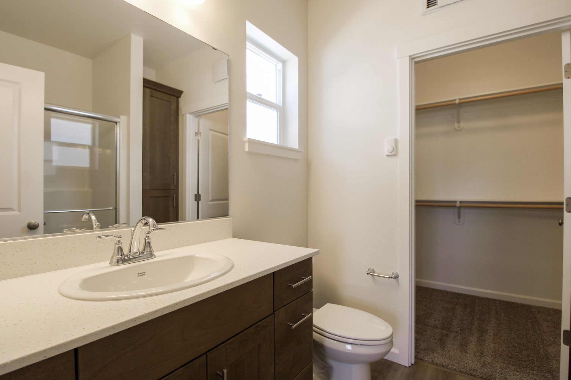 A bathroom with a sink , toilet , mirror and walk in closet.