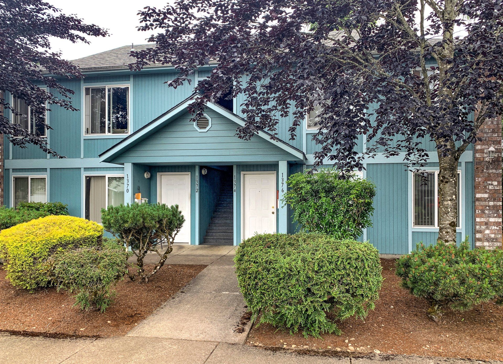 A blue apartment building with stairs and bushes in front of it