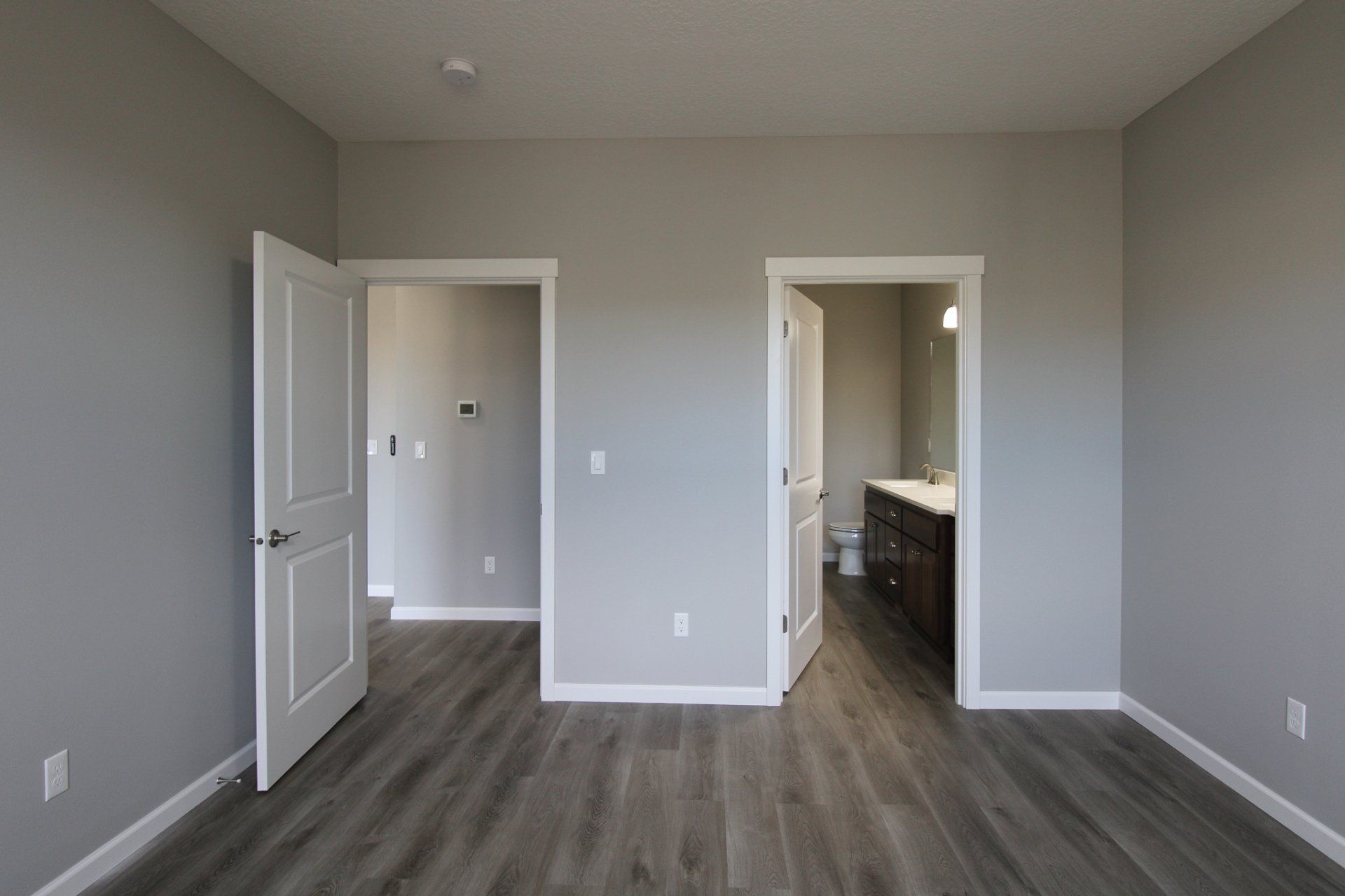 An empty bedroom with hardwood floors and gray walls.
