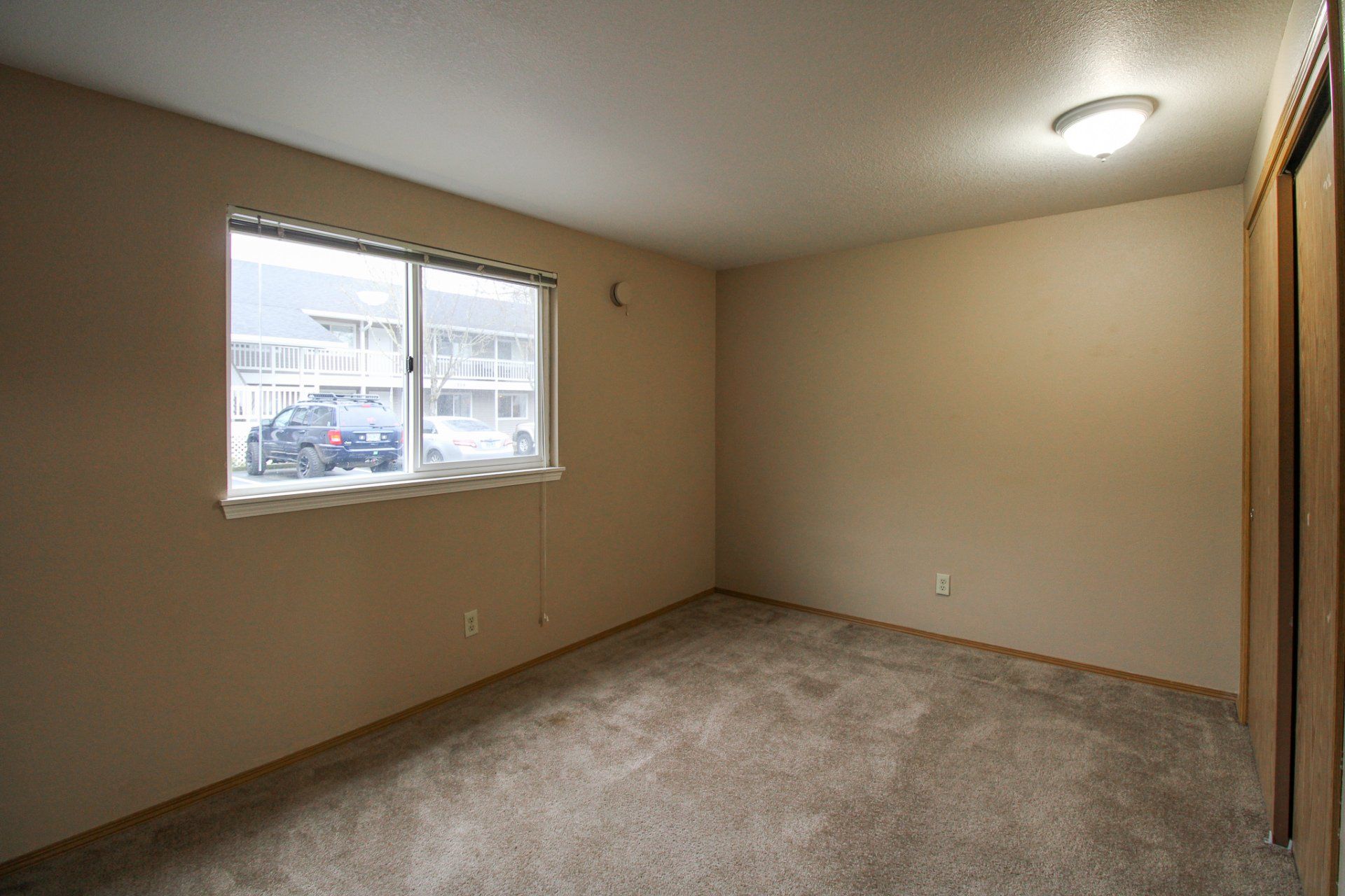 An empty bedroom with a window and a carpeted floor.