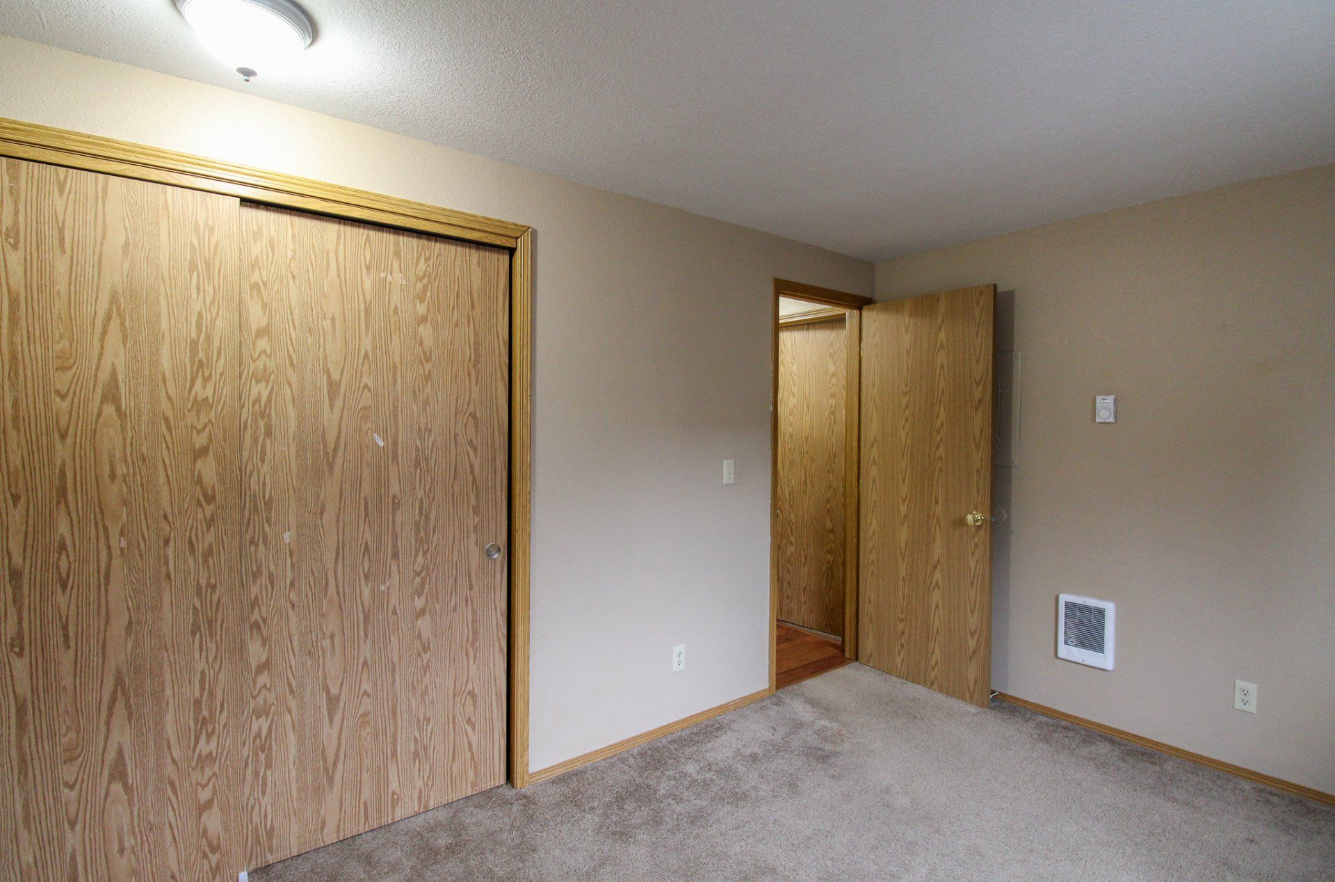 An empty bedroom with a carpeted floor and wooden doors.