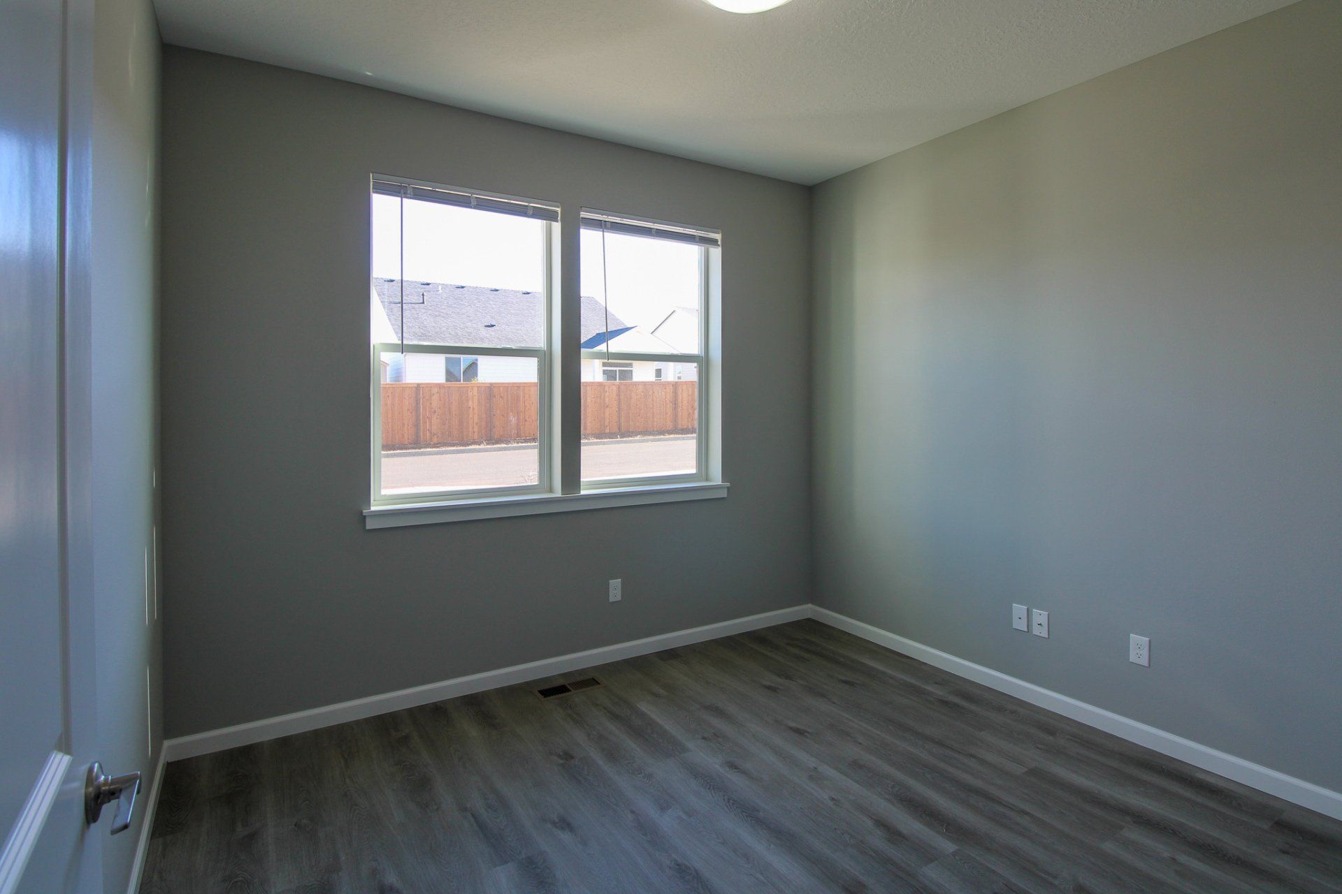 An empty bedroom with hardwood floors and two windows.