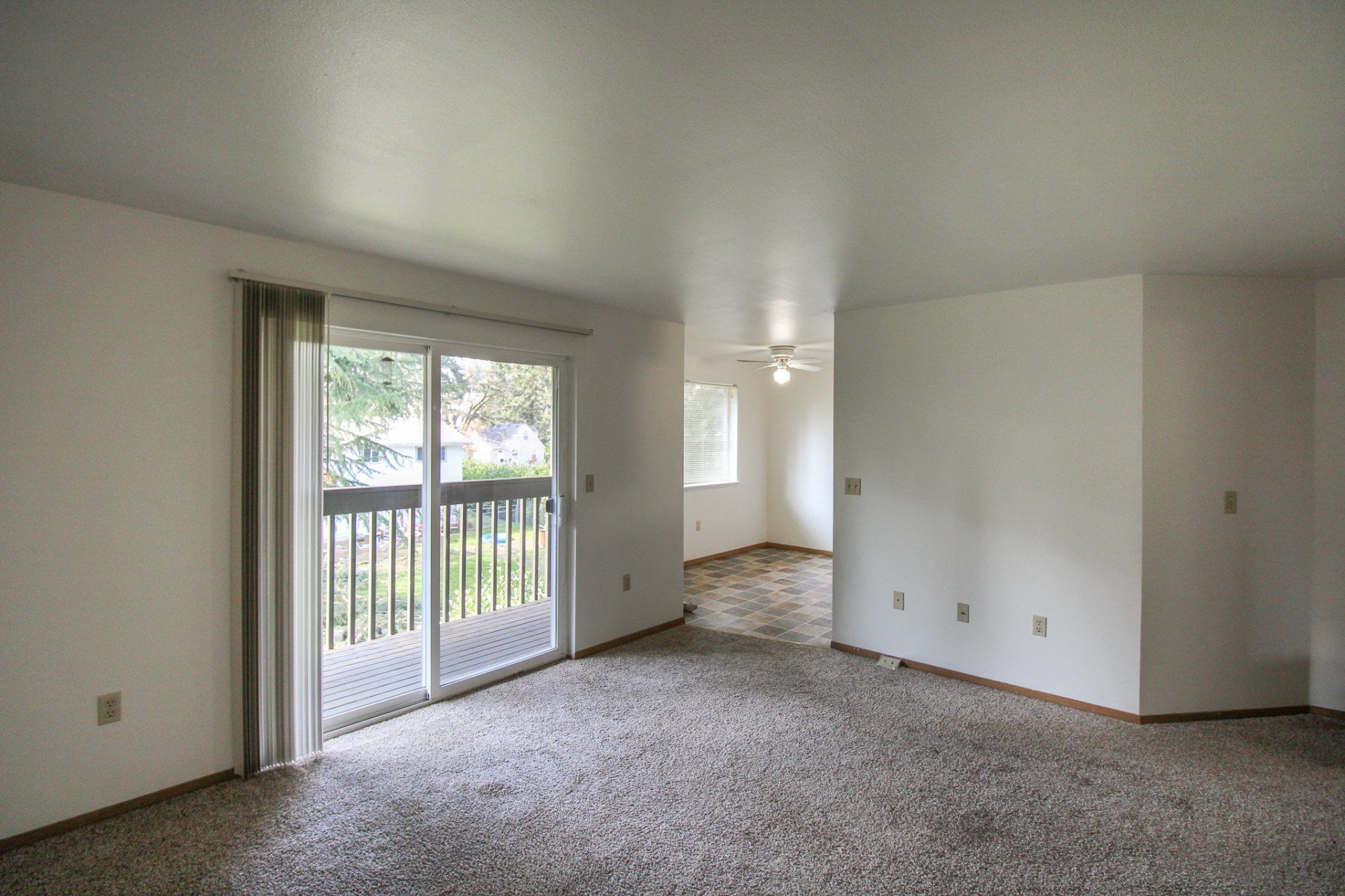An empty living room with a sliding glass door and a balcony.