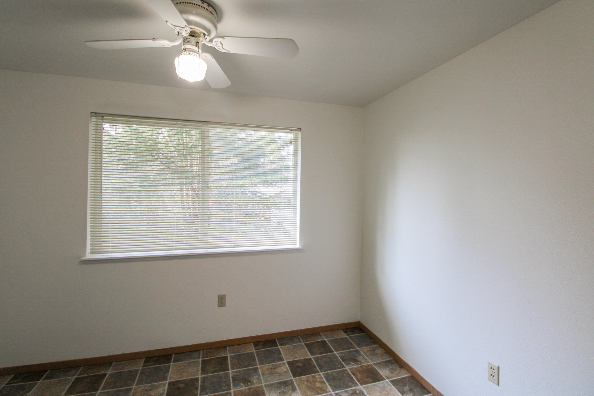 An empty room with a ceiling fan and a window.