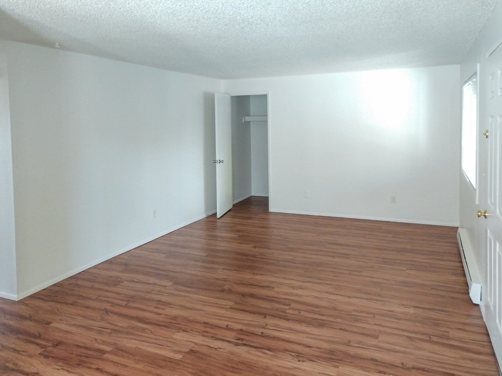 An empty living room with hardwood floors and white walls.