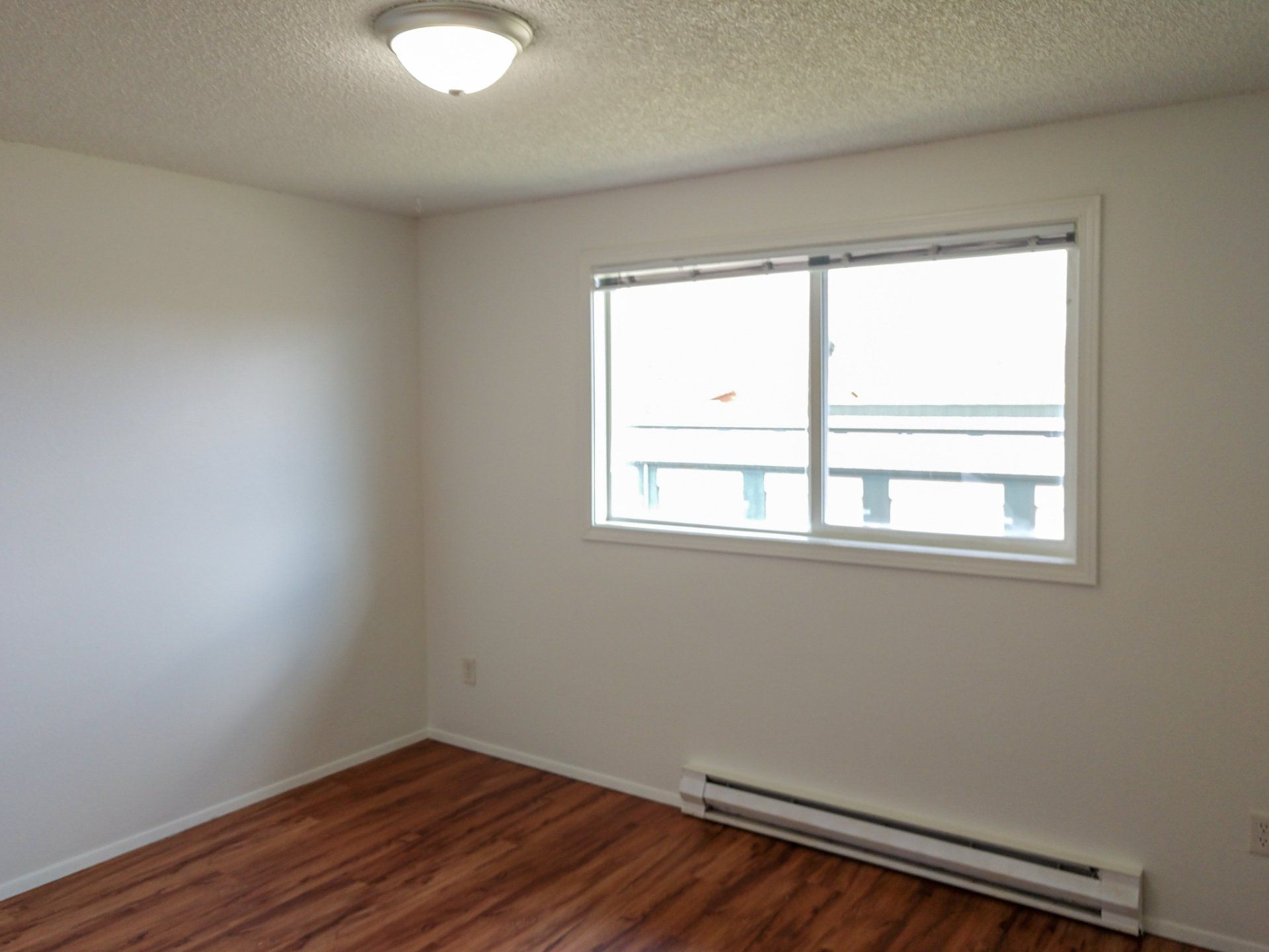 An empty bedroom with hardwood floors and a large window.