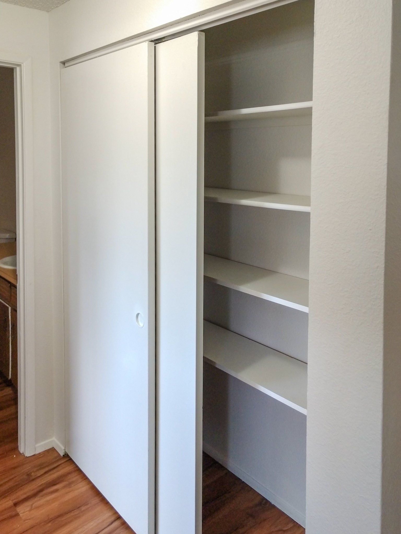 A closet with sliding doors and shelves in a hallway.