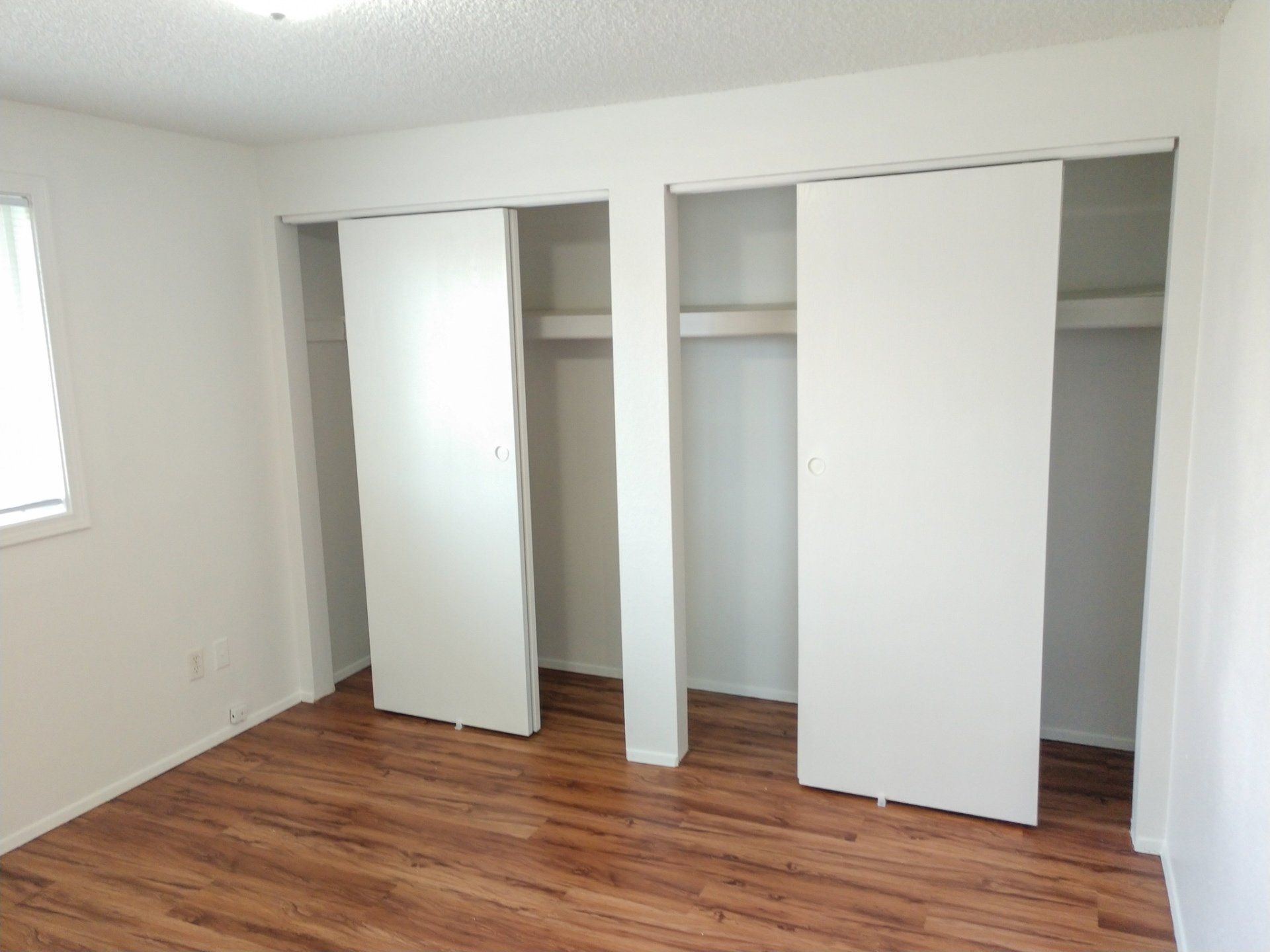 A bedroom with hardwood floors and white closet doors