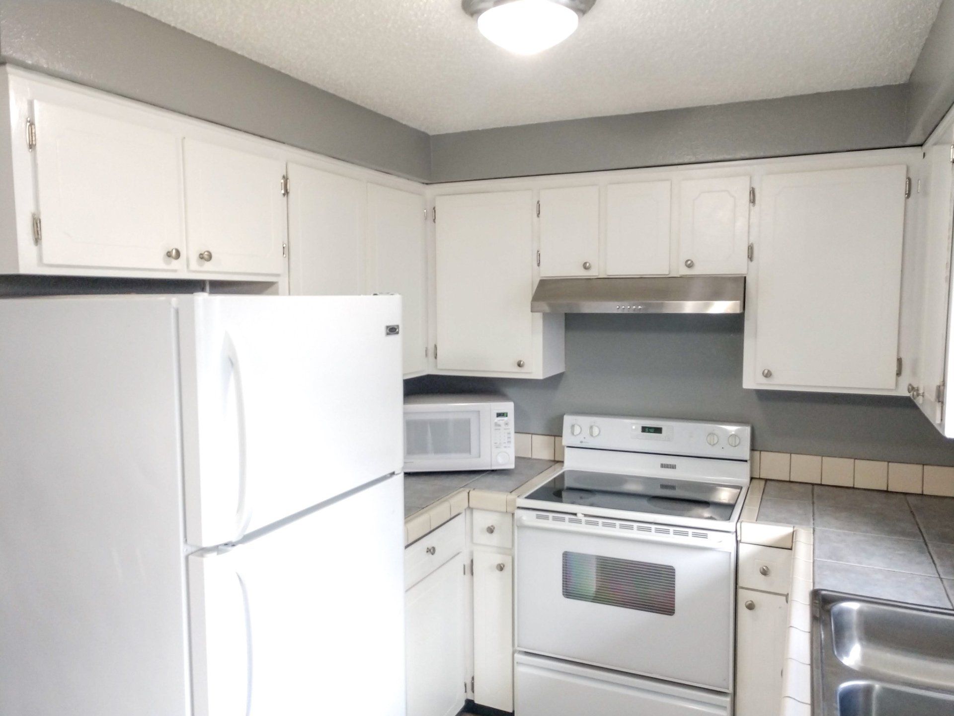 A kitchen with white cabinets a stove a refrigerator and a microwave