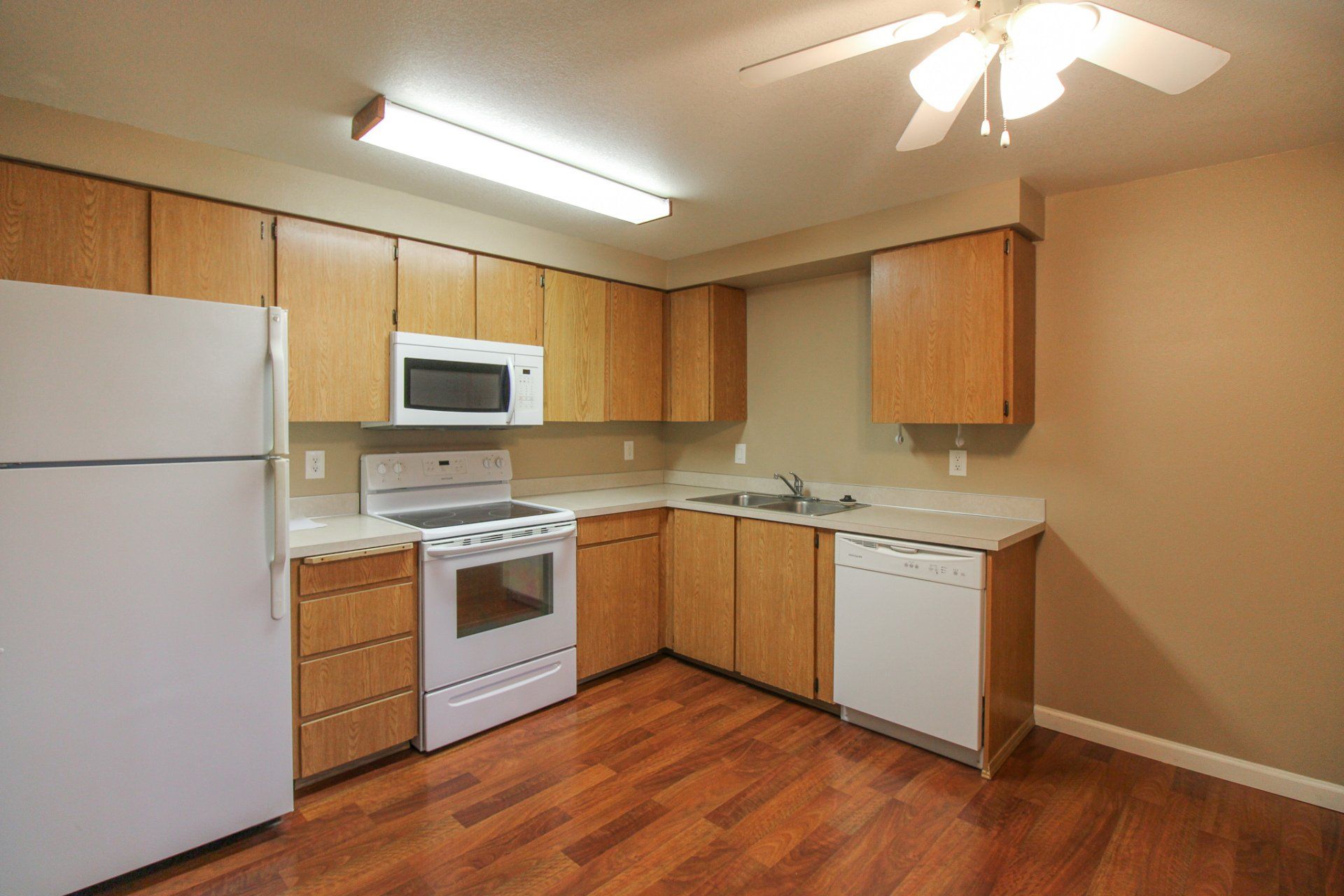 An empty kitchen with wooden cabinets and white appliances