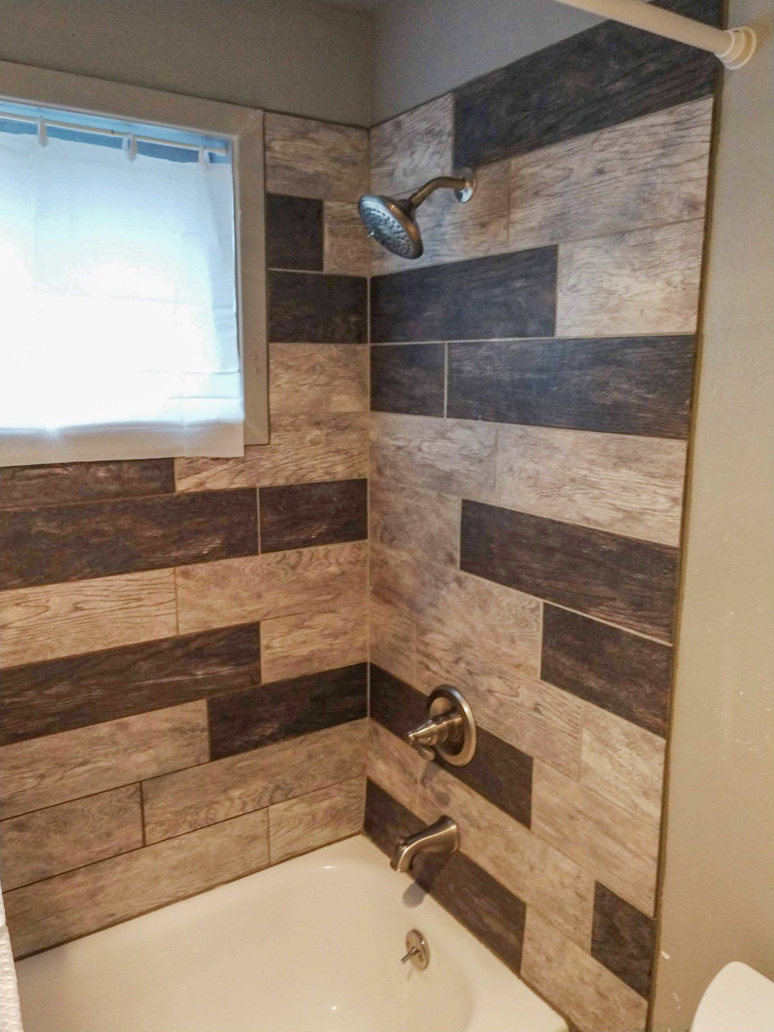A bathroom with a tub , shower , toilet and window.