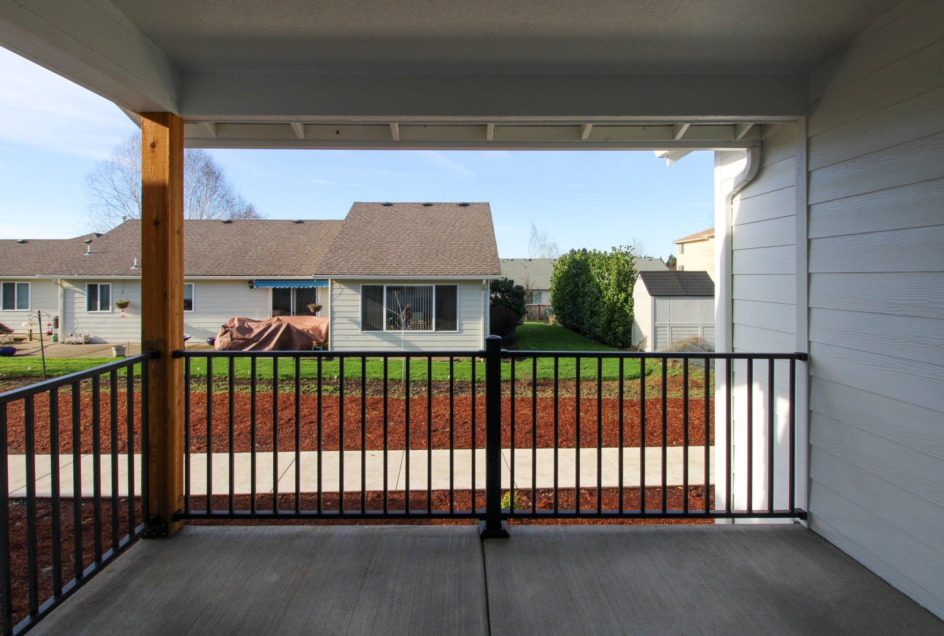 An empty porch with a metal railing and a house in the background