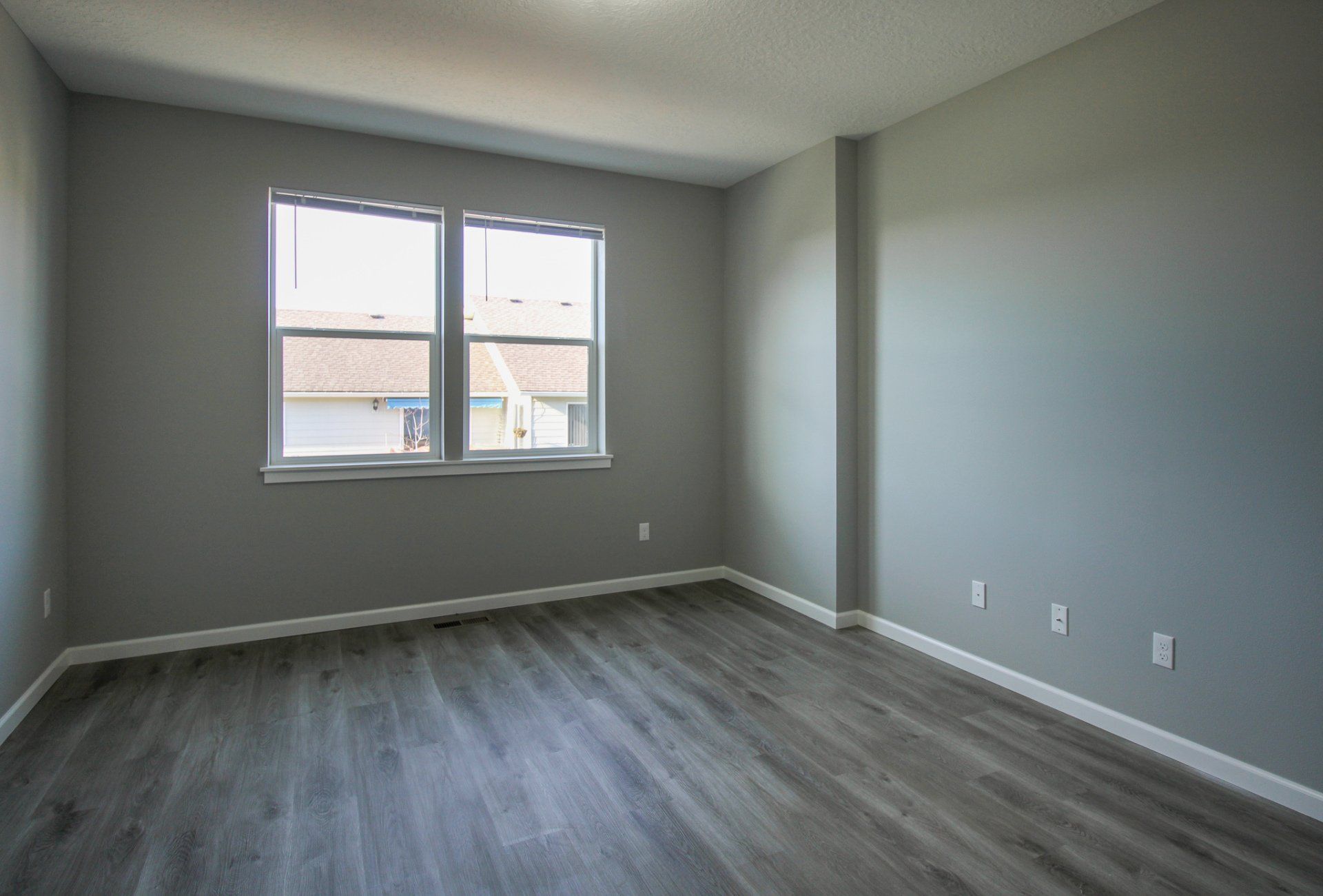 An empty bedroom with hardwood floors and two windows.