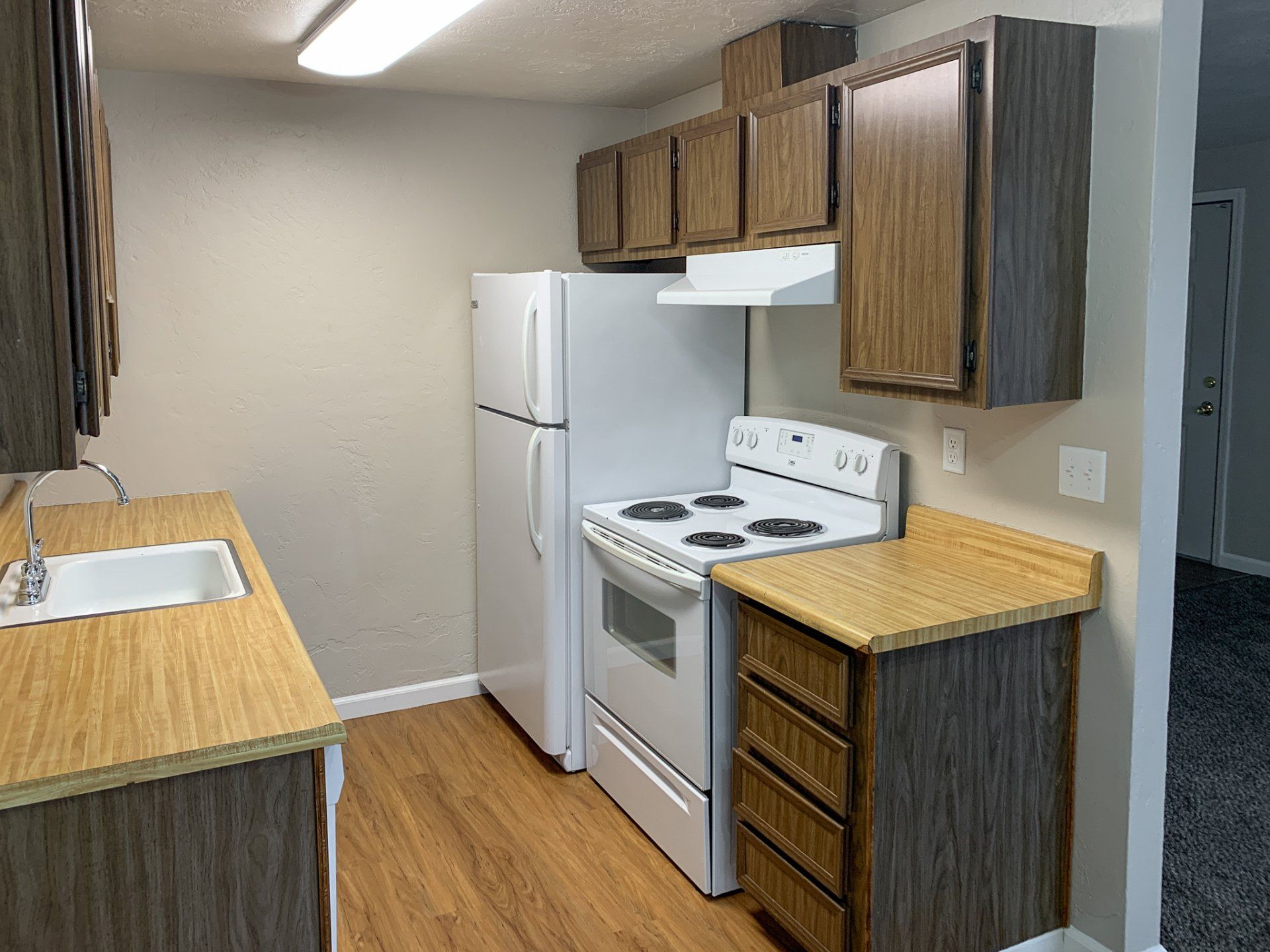 A kitchen with a stove , refrigerator , sink and cabinets.