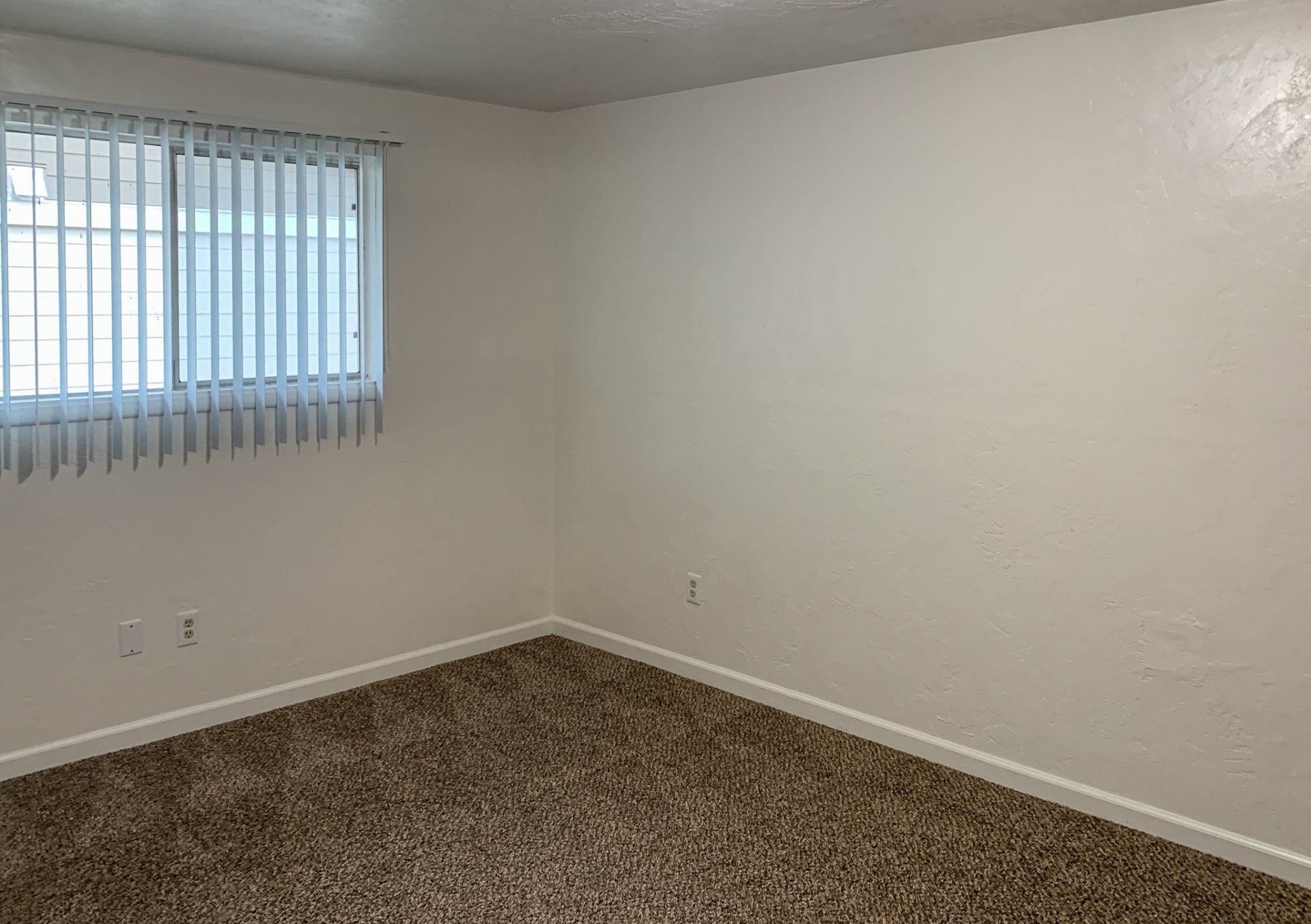 An empty bedroom with a large window and blinds.