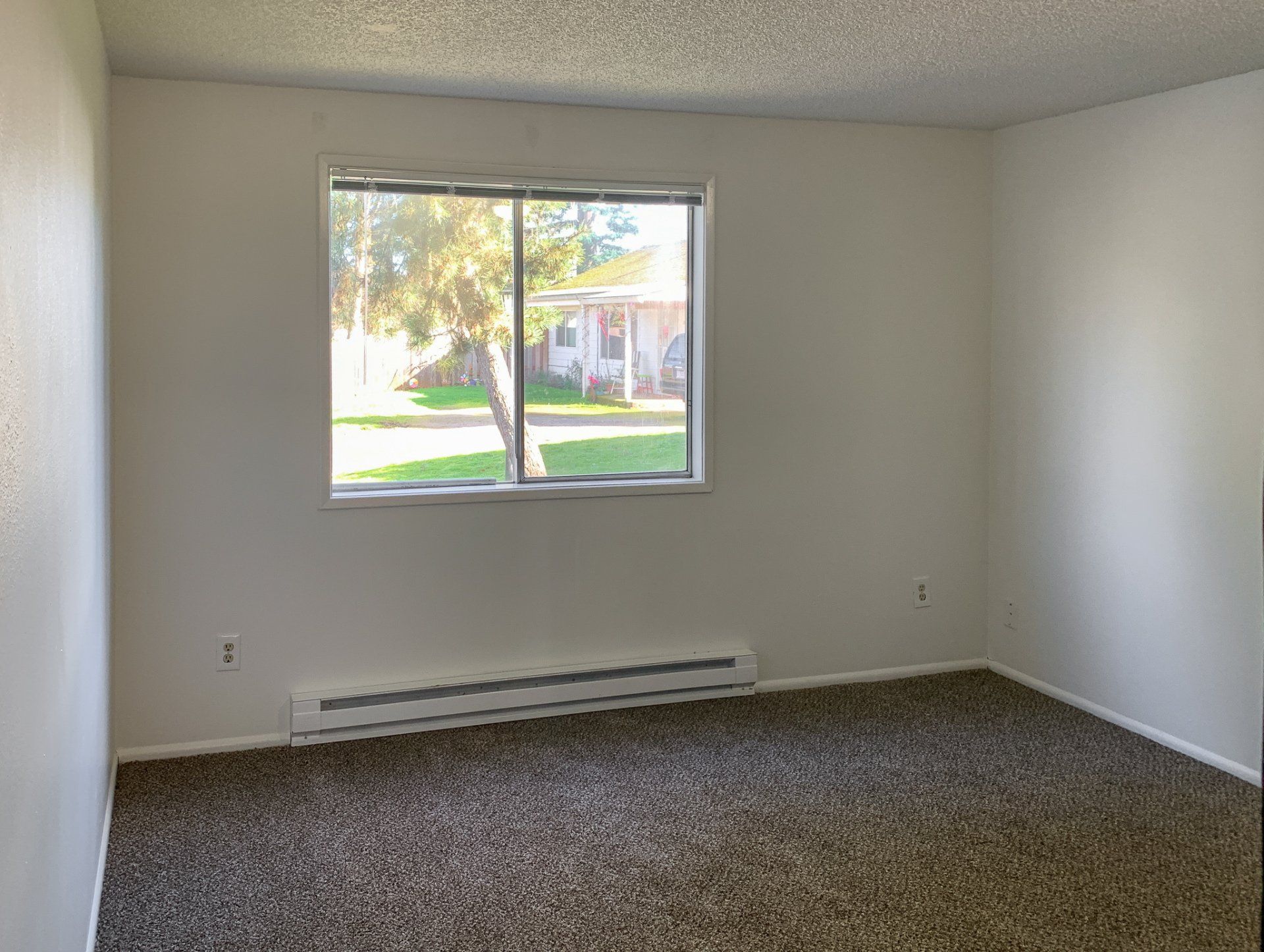 An empty living room with a large window and a sliding glass door.