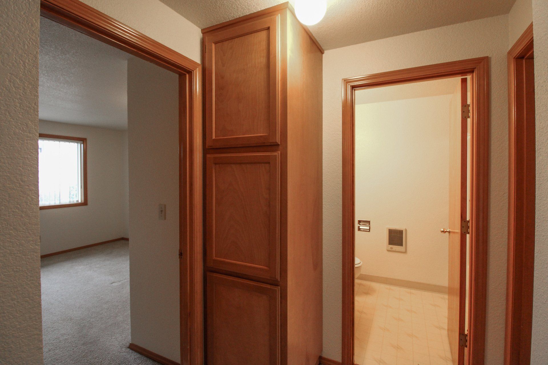 A hallway with wooden cabinets and a door leading to a bathroom.