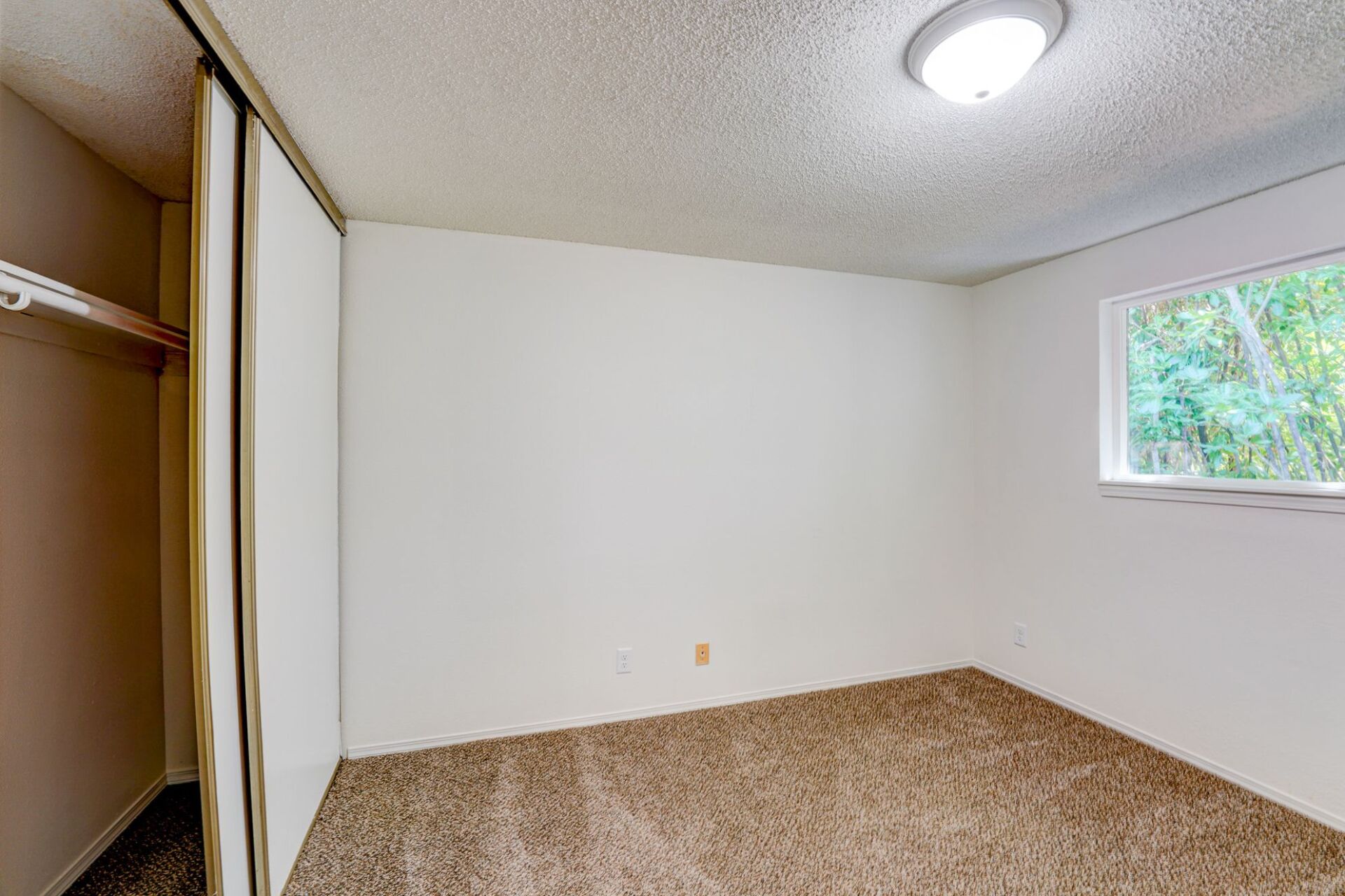 An empty bedroom with a closet and a window.
