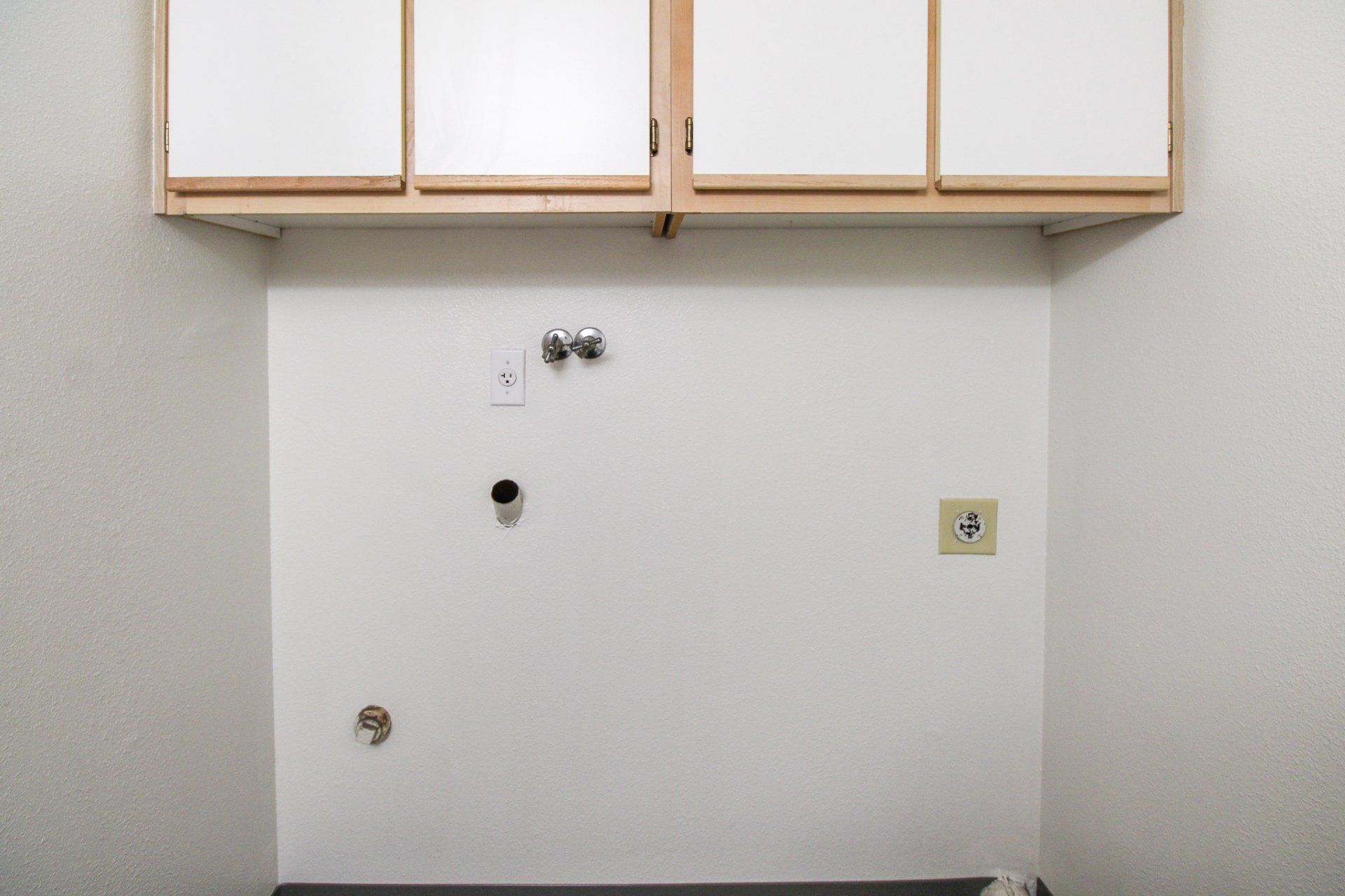 An empty laundry room with white cabinets and a sink.
