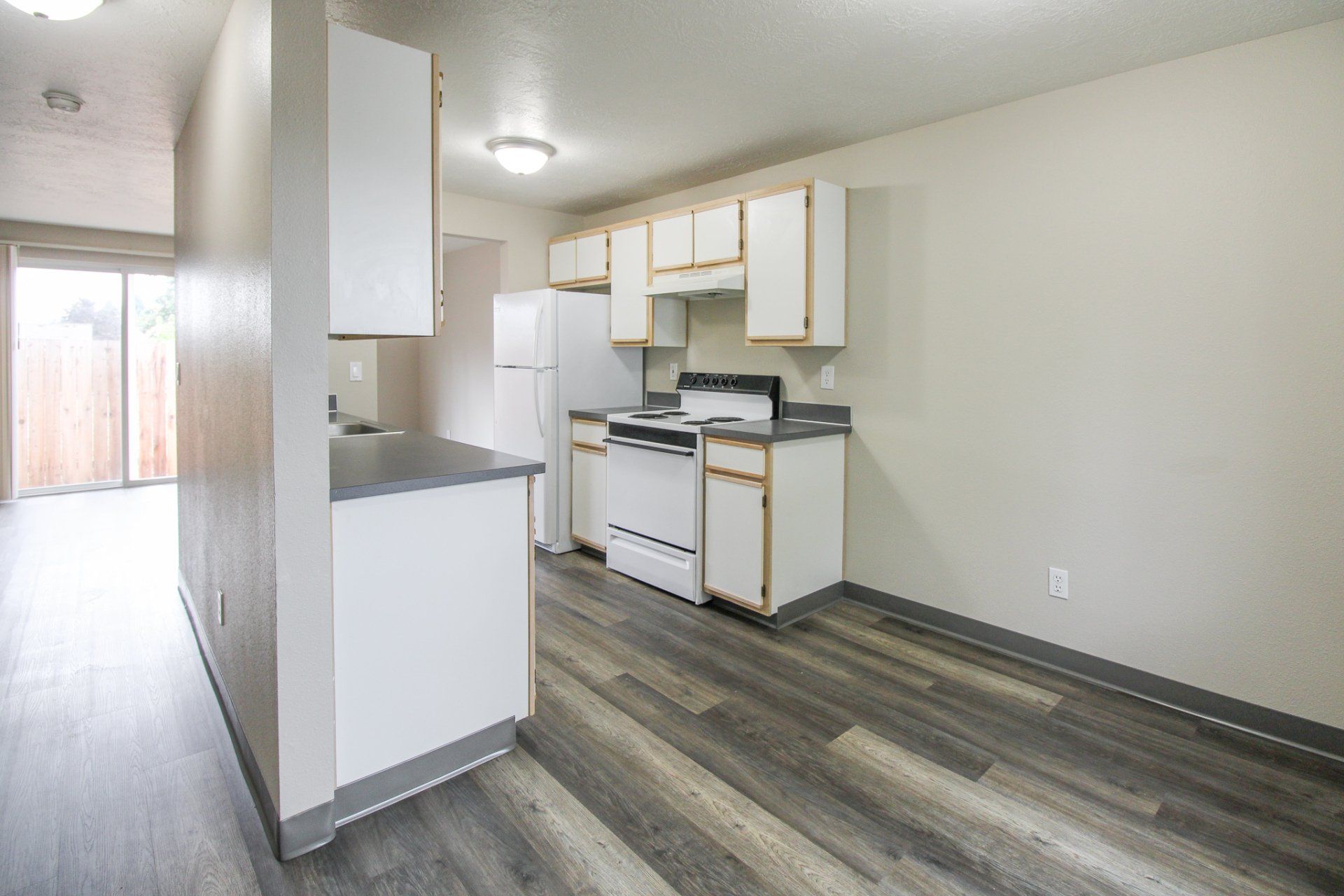 A kitchen with a stove , refrigerator , cabinets and hardwood floors.