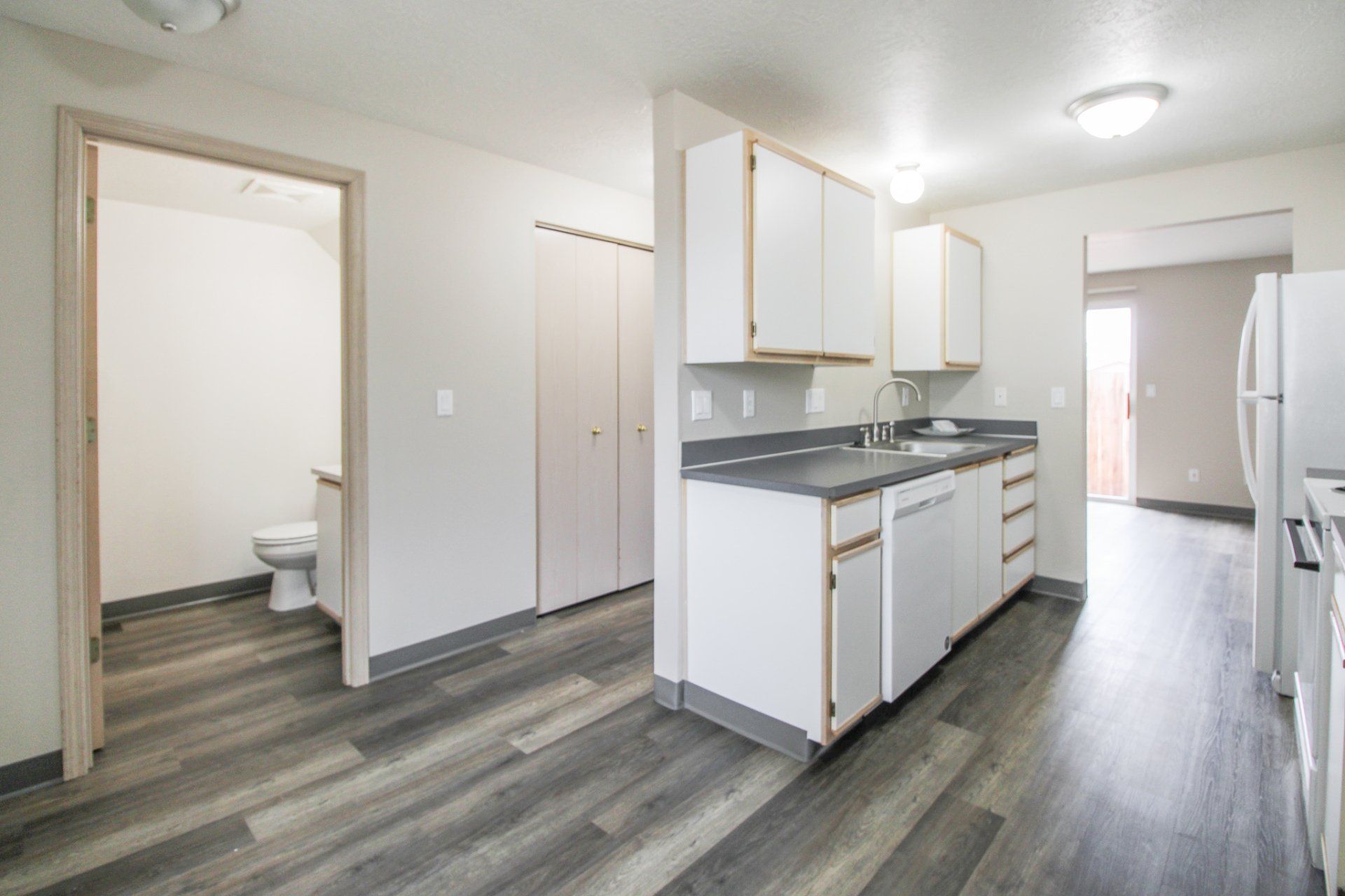 A kitchen with white cabinets , a refrigerator , a sink , and a toilet.
