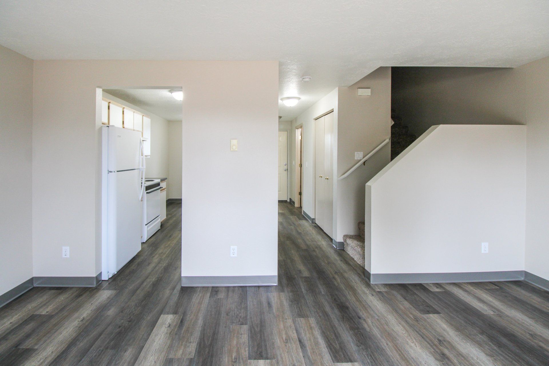 A living room with hardwood floors and a staircase leading to the kitchen.