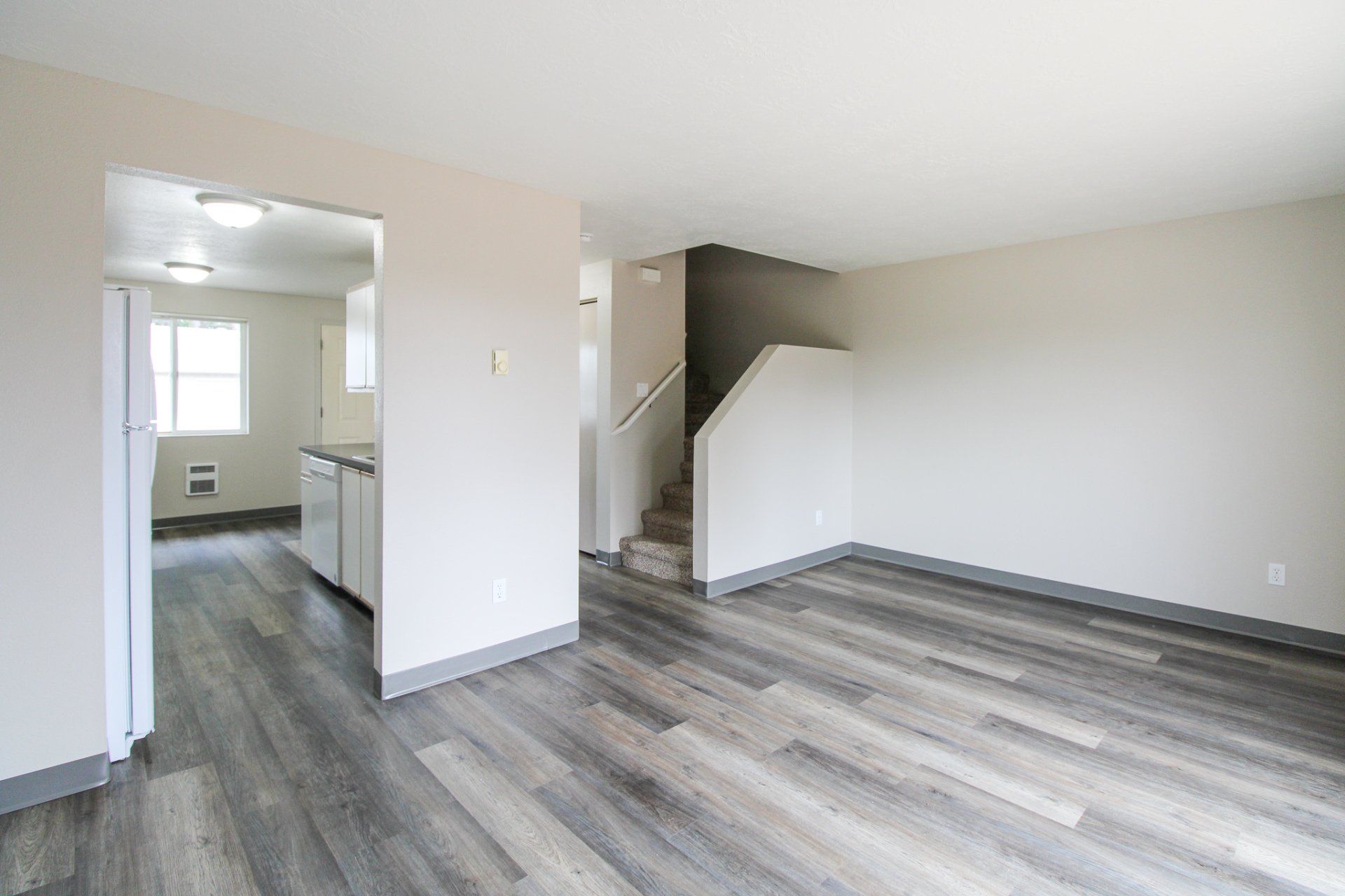 An empty living room with hardwood floors and stairs leading to the kitchen.