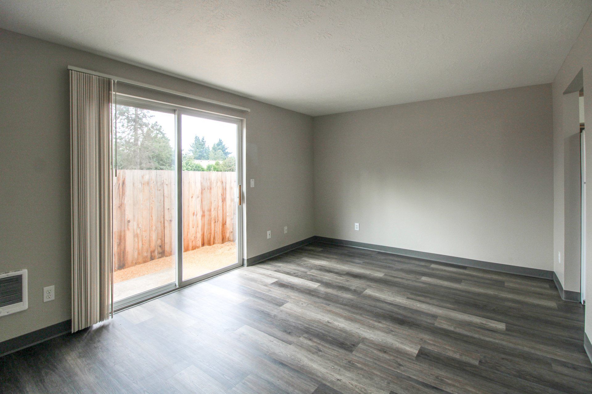 An empty living room with a sliding glass door and hardwood floors.
