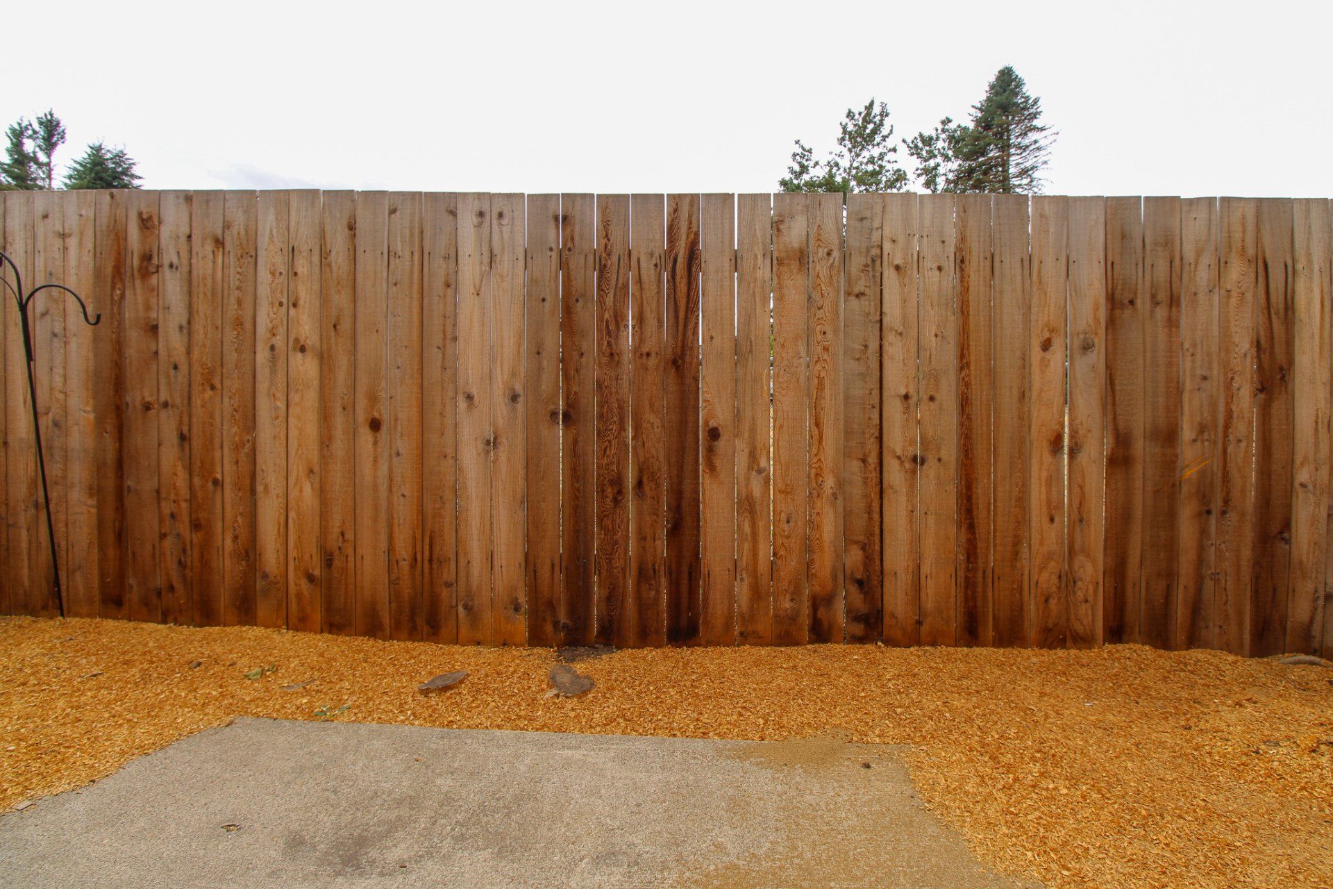 A wooden fence surrounds a gravel area with trees in the background.