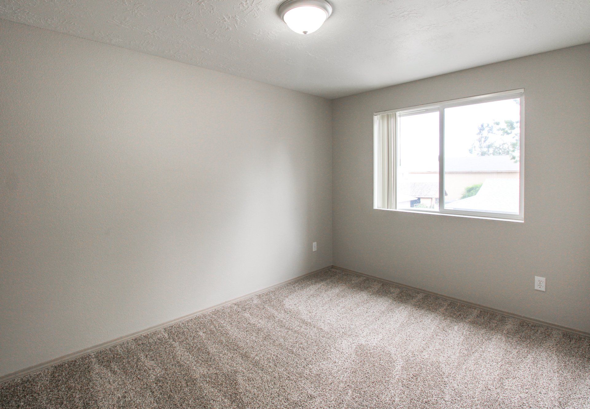 An empty bedroom with a carpeted floor and a window.