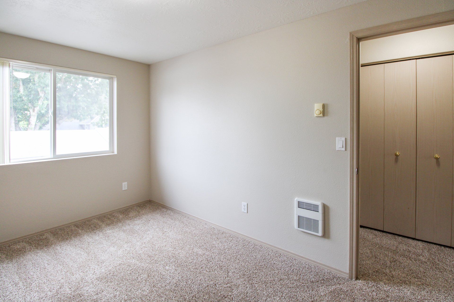 An empty room with a carpeted floor and a window.
