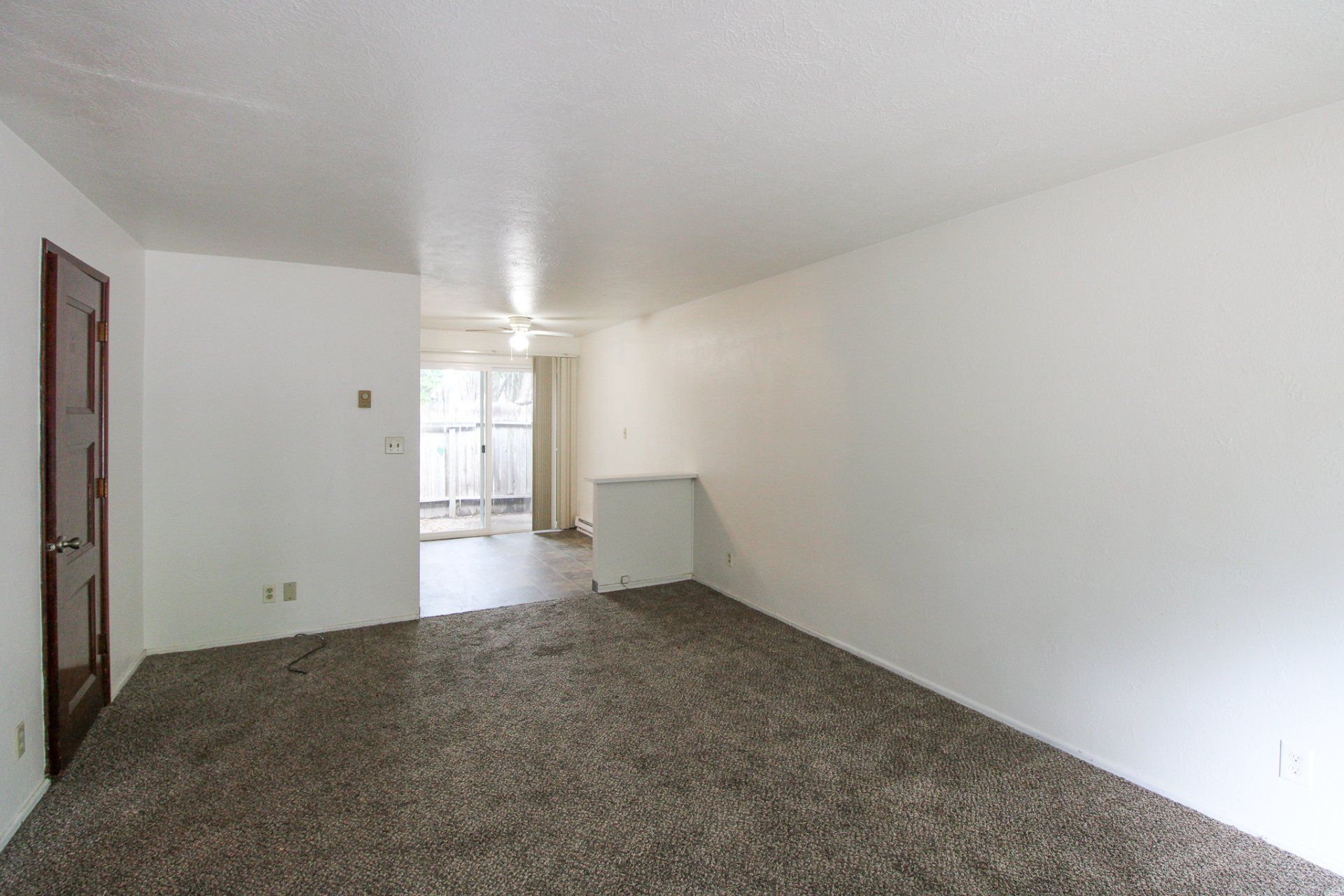 An empty living room with a brown carpet and white walls.
