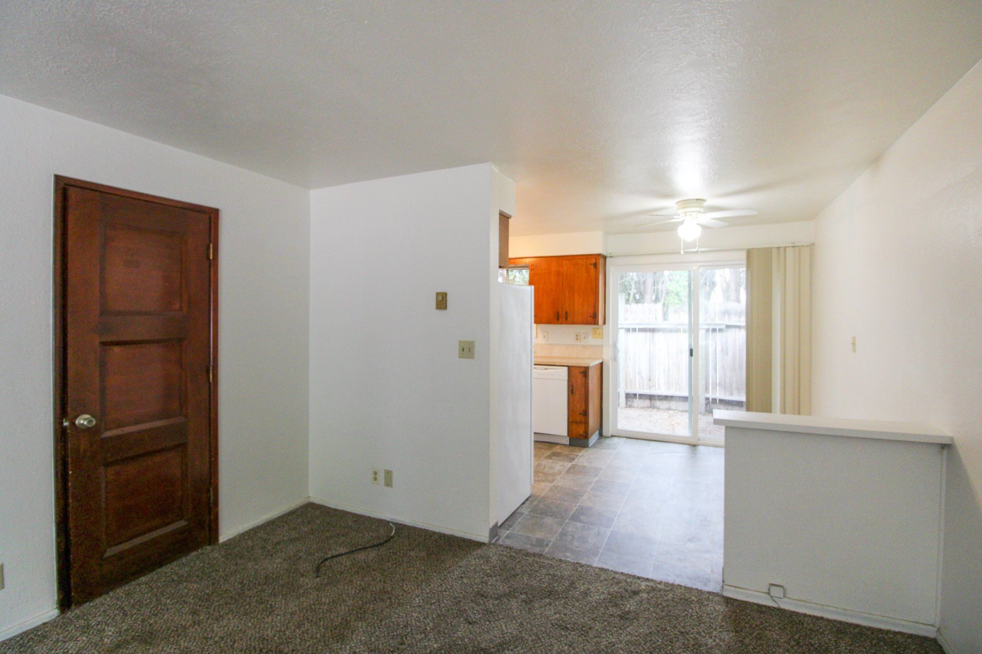 An empty living room with a sliding glass door leading to a kitchen.