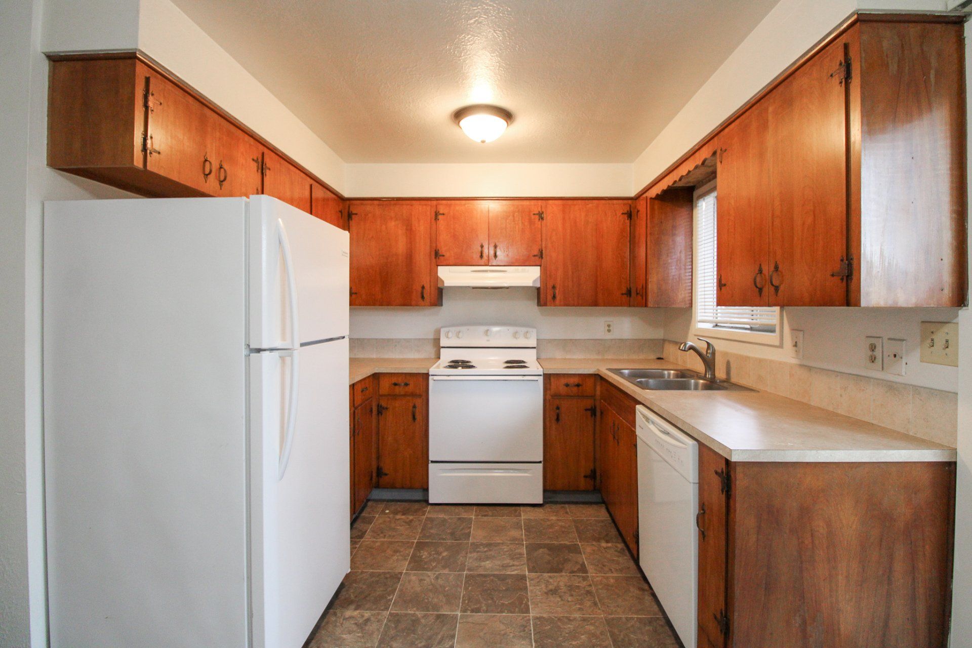 An empty kitchen with wooden cabinets and a white refrigerator