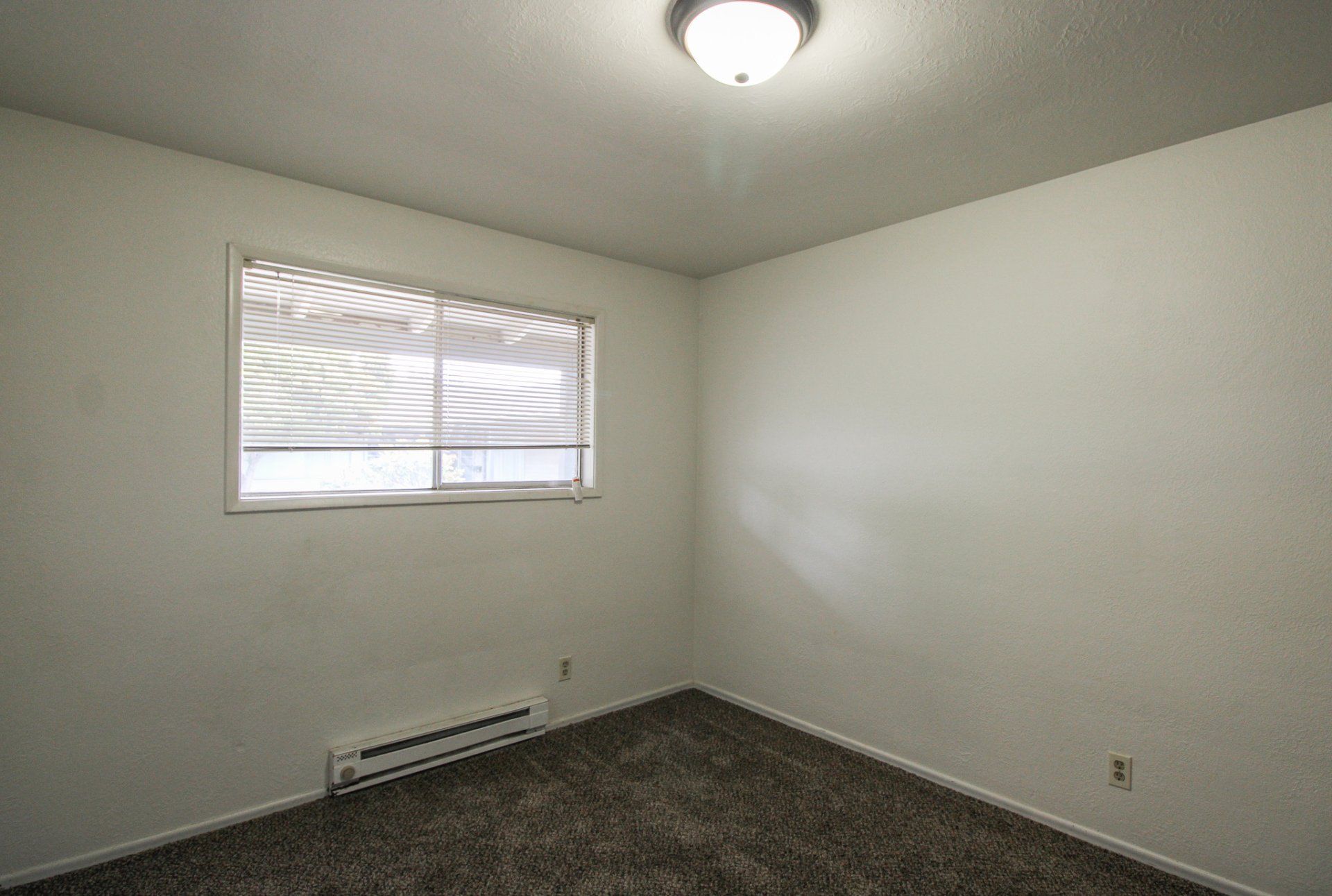 An empty bedroom with a window and a ceiling light.