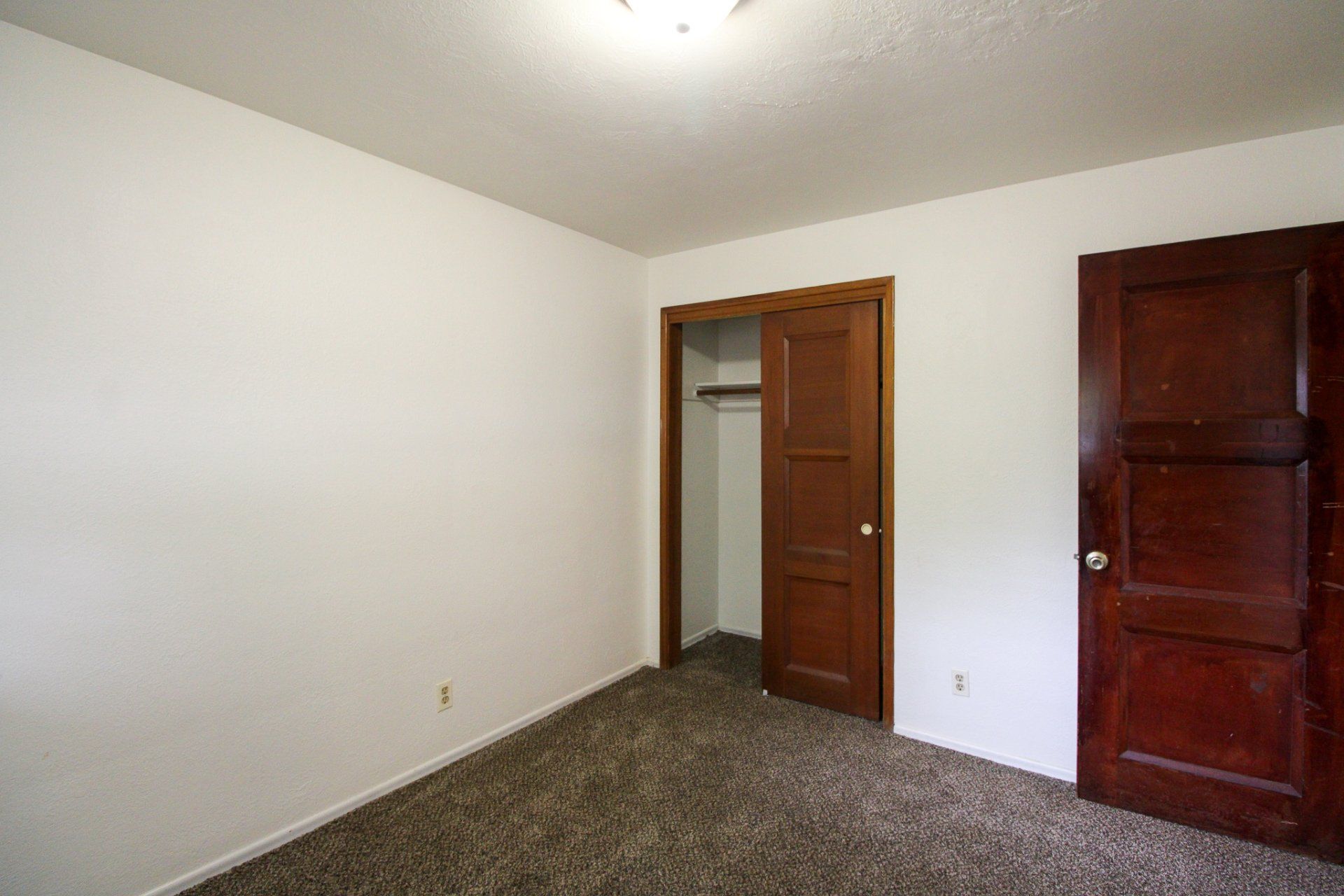 An empty bedroom with a closet and two doors.
