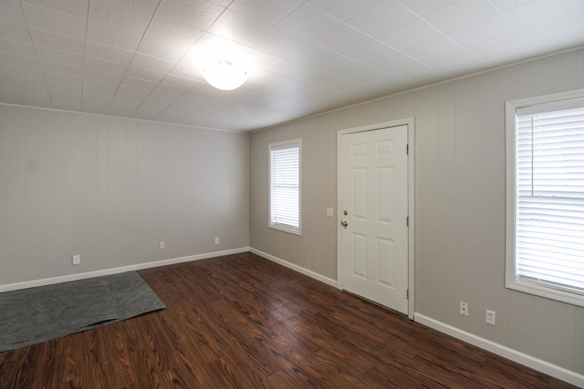 An empty living room with hardwood floors and two windows.