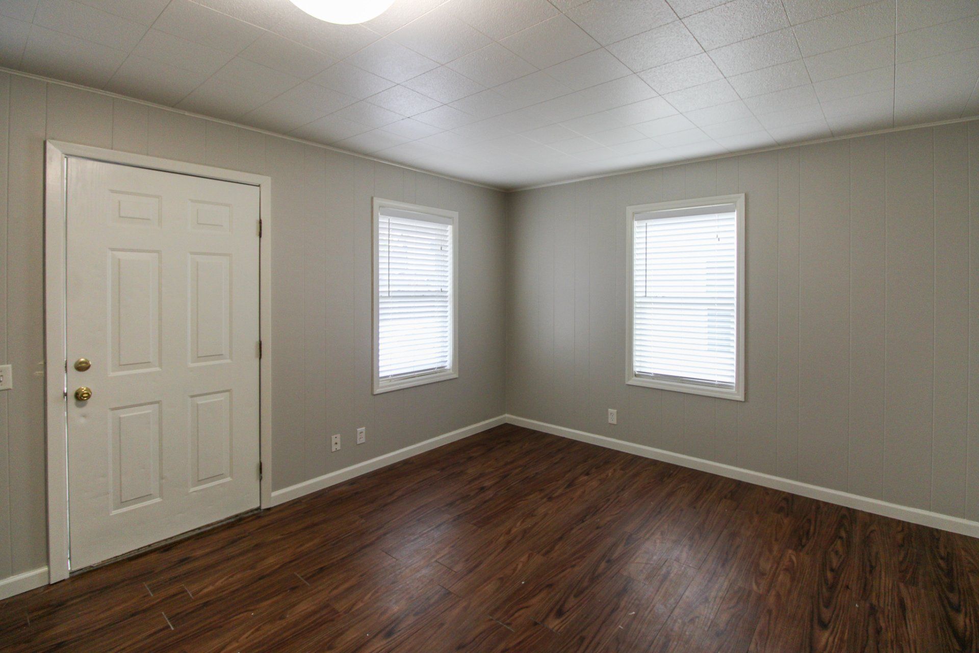 An empty living room with hardwood floors and two windows.