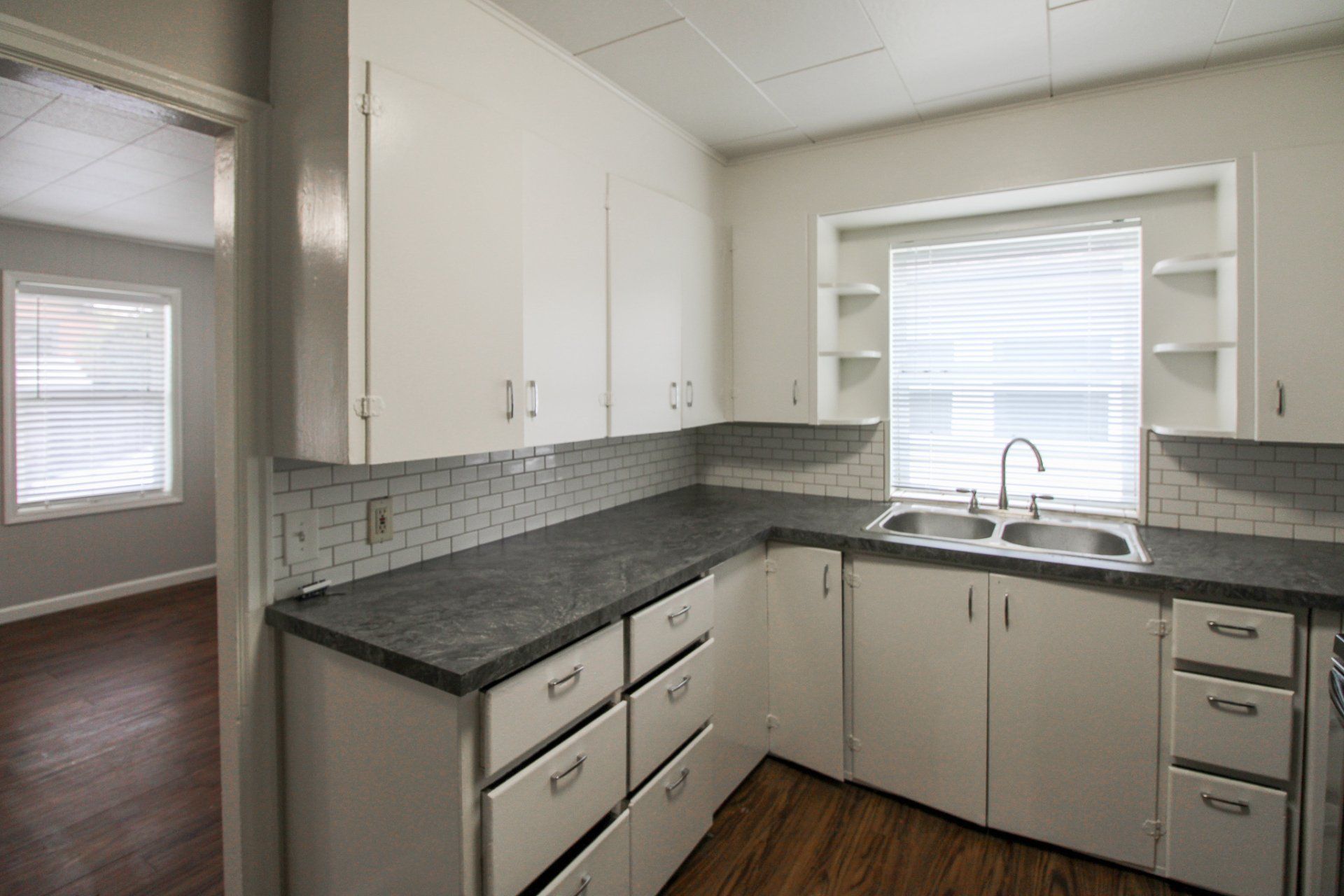 A kitchen with white cabinets , granite counter tops , a sink and a window.