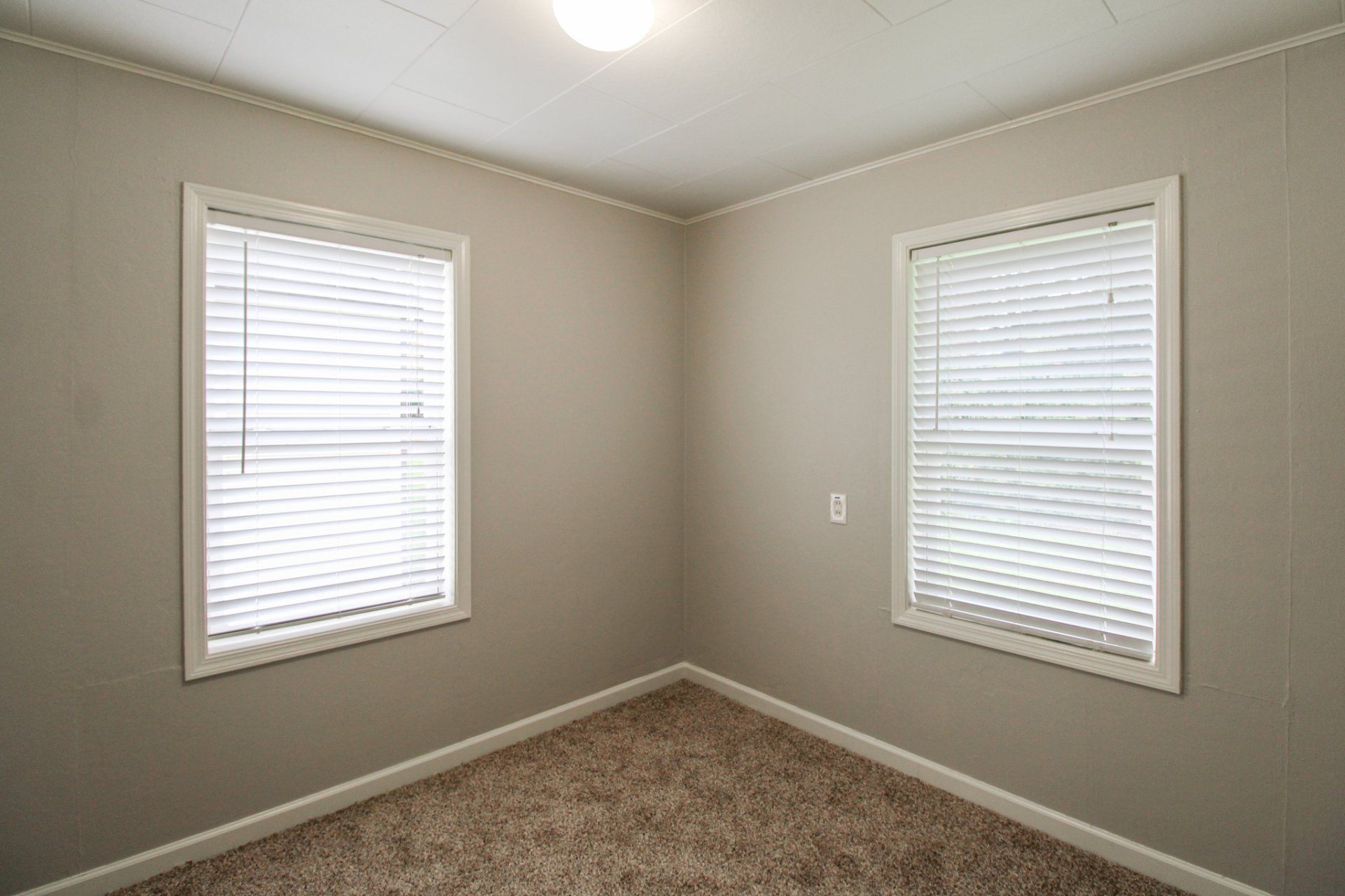 An empty room with two windows and blinds on the windows.