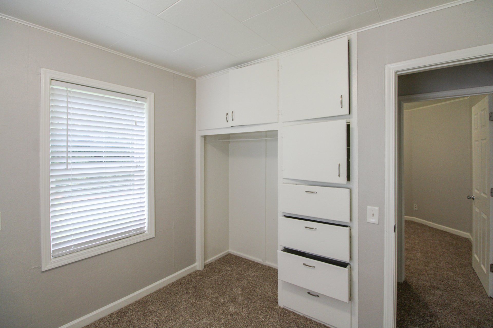 An empty bedroom with white cabinets and drawers and a window.