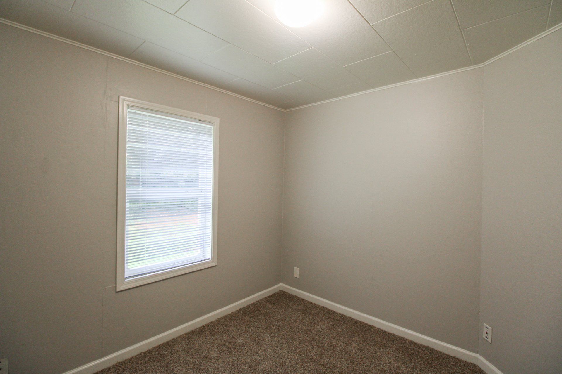 An empty bedroom with a window and carpet.