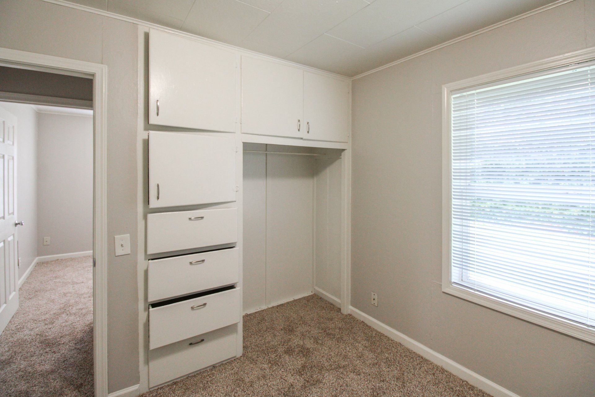 An empty bedroom with white cabinets and drawers and a window.