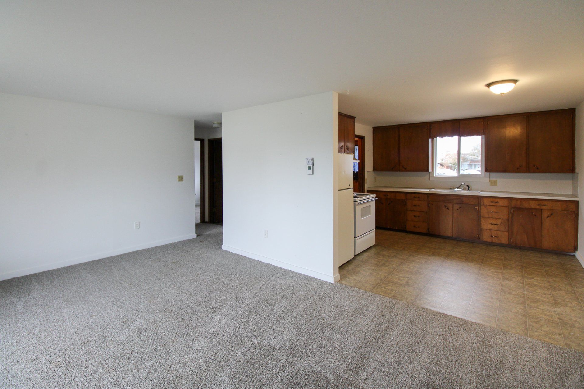 An empty living room with a kitchen in the background.