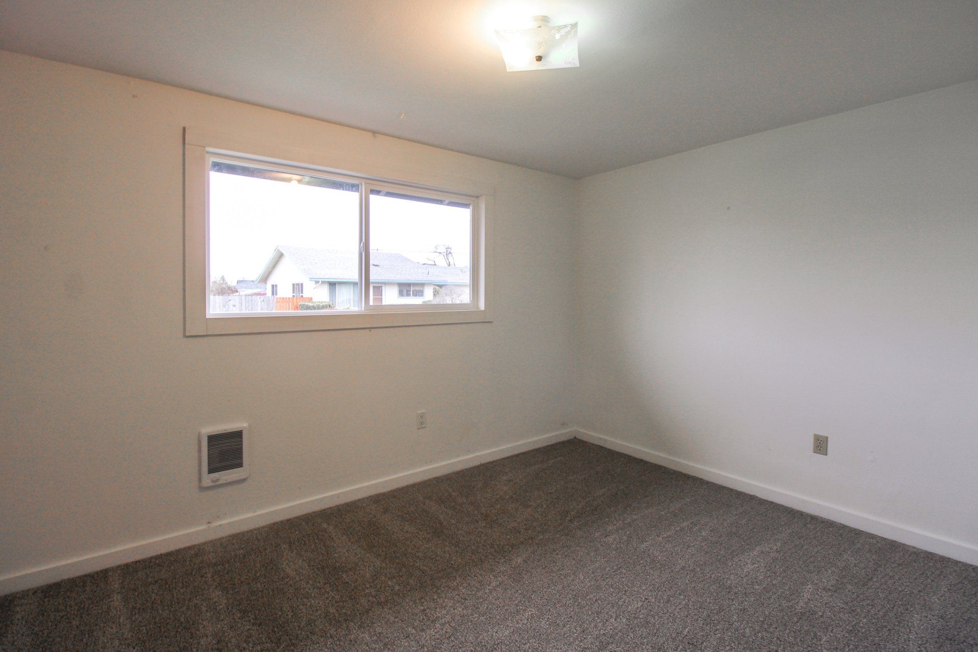 An empty room with a window and a carpeted floor.