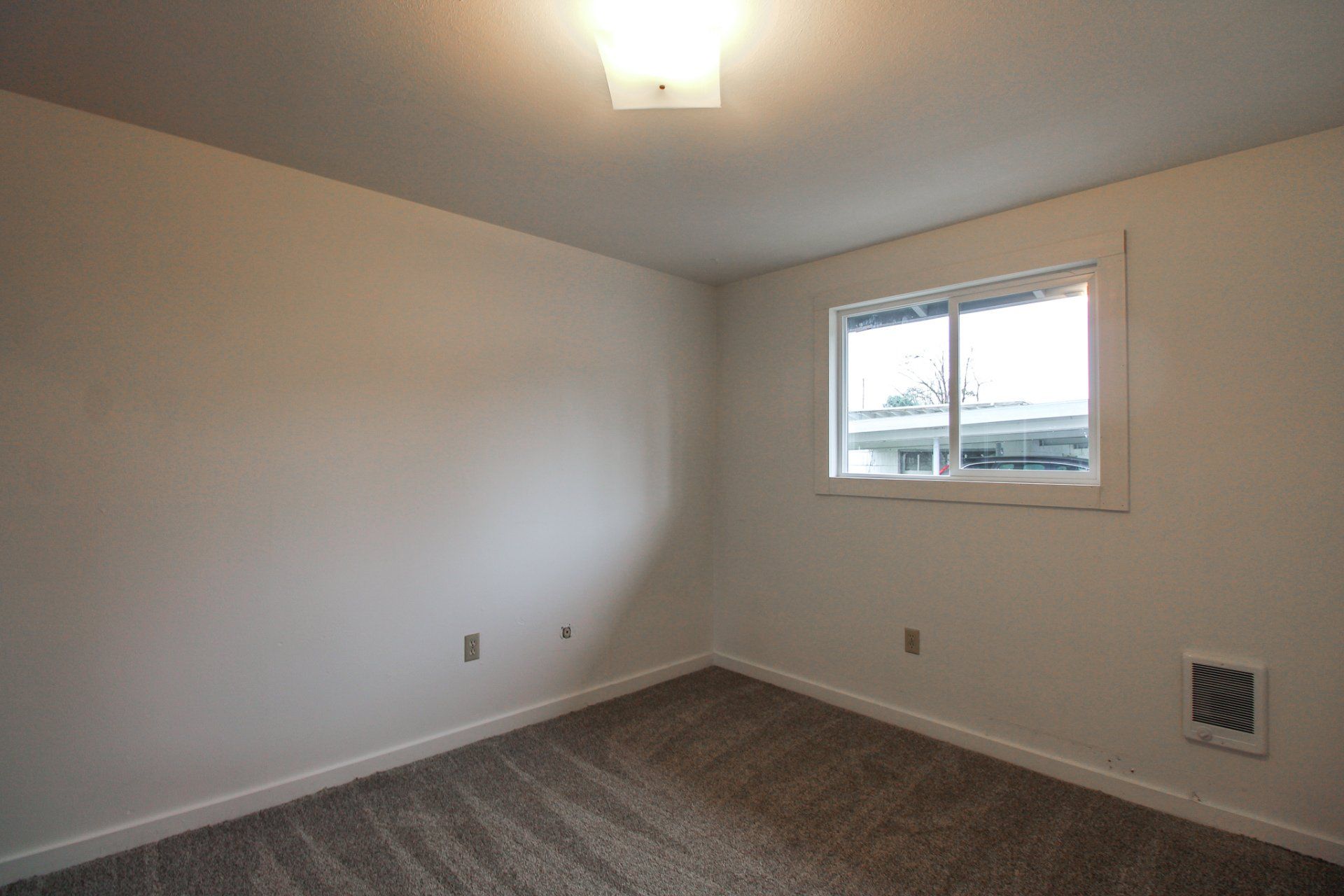 An empty bedroom with a window and carpet.