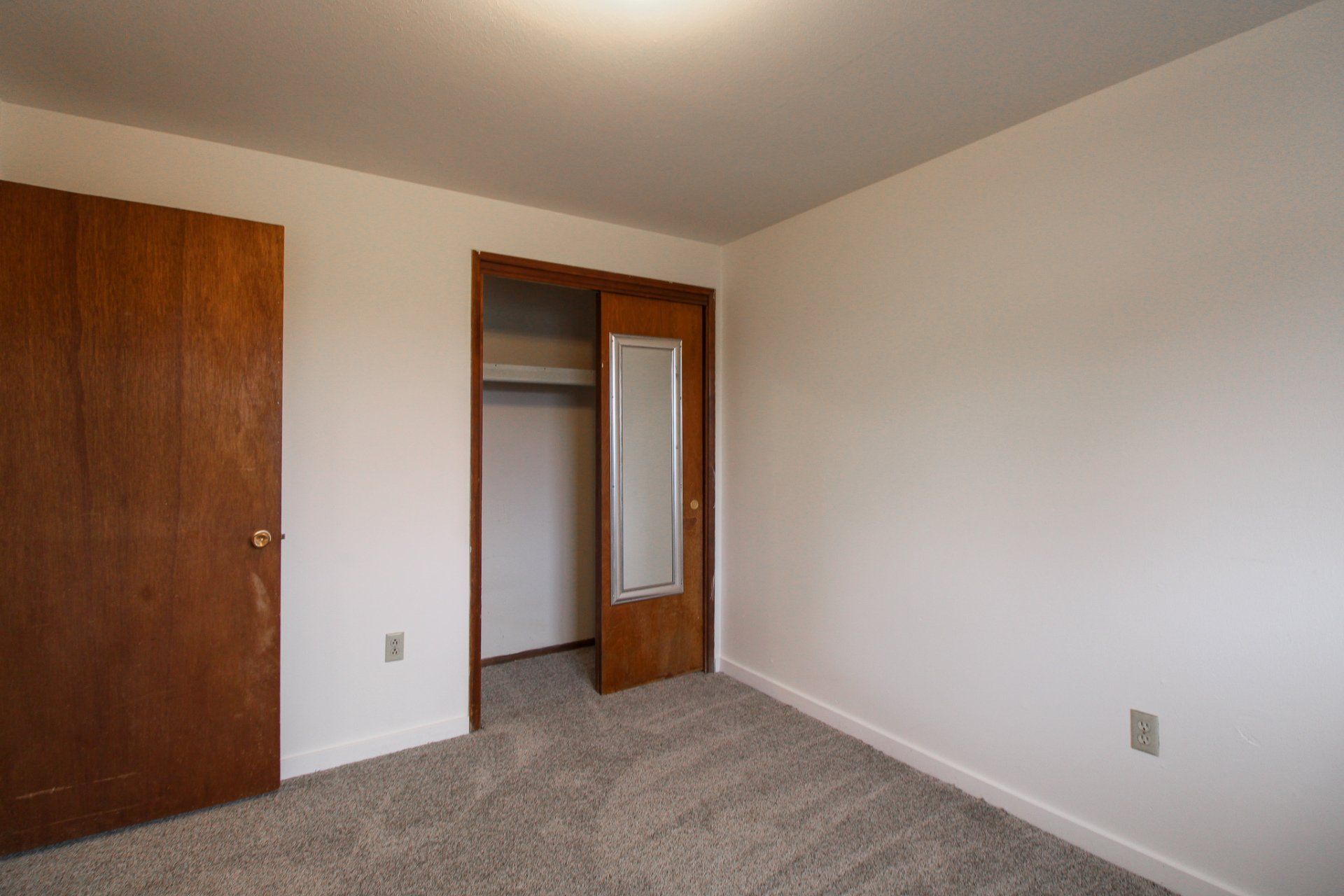 An empty bedroom with a closet and a mirror.